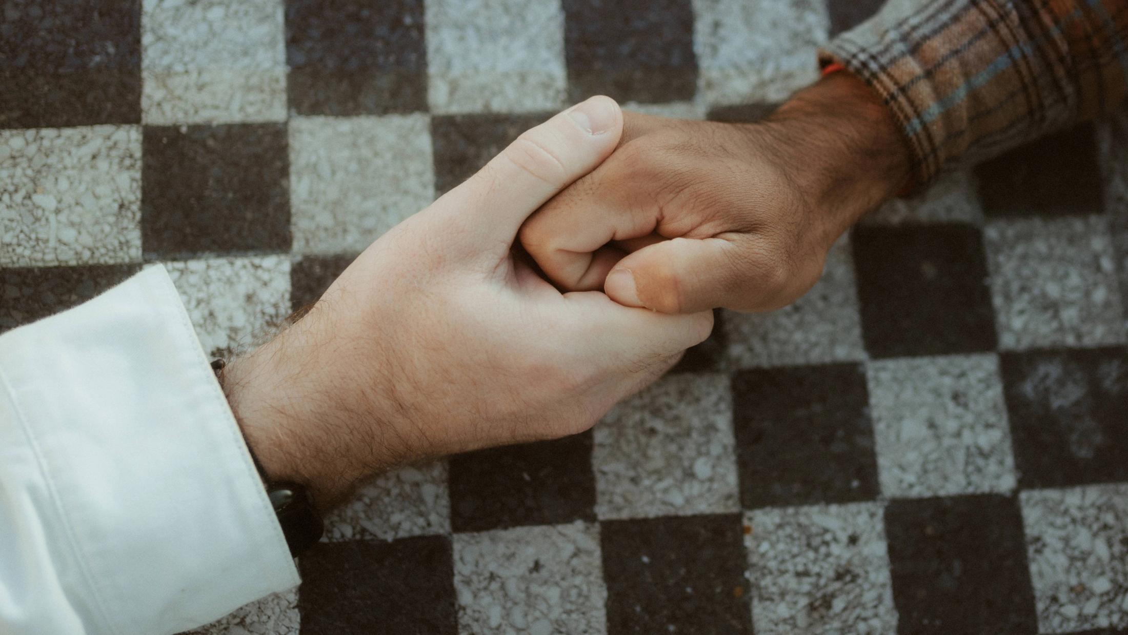 Close view of Kris and Ilya holding hands above a black-and-white checkered surface.