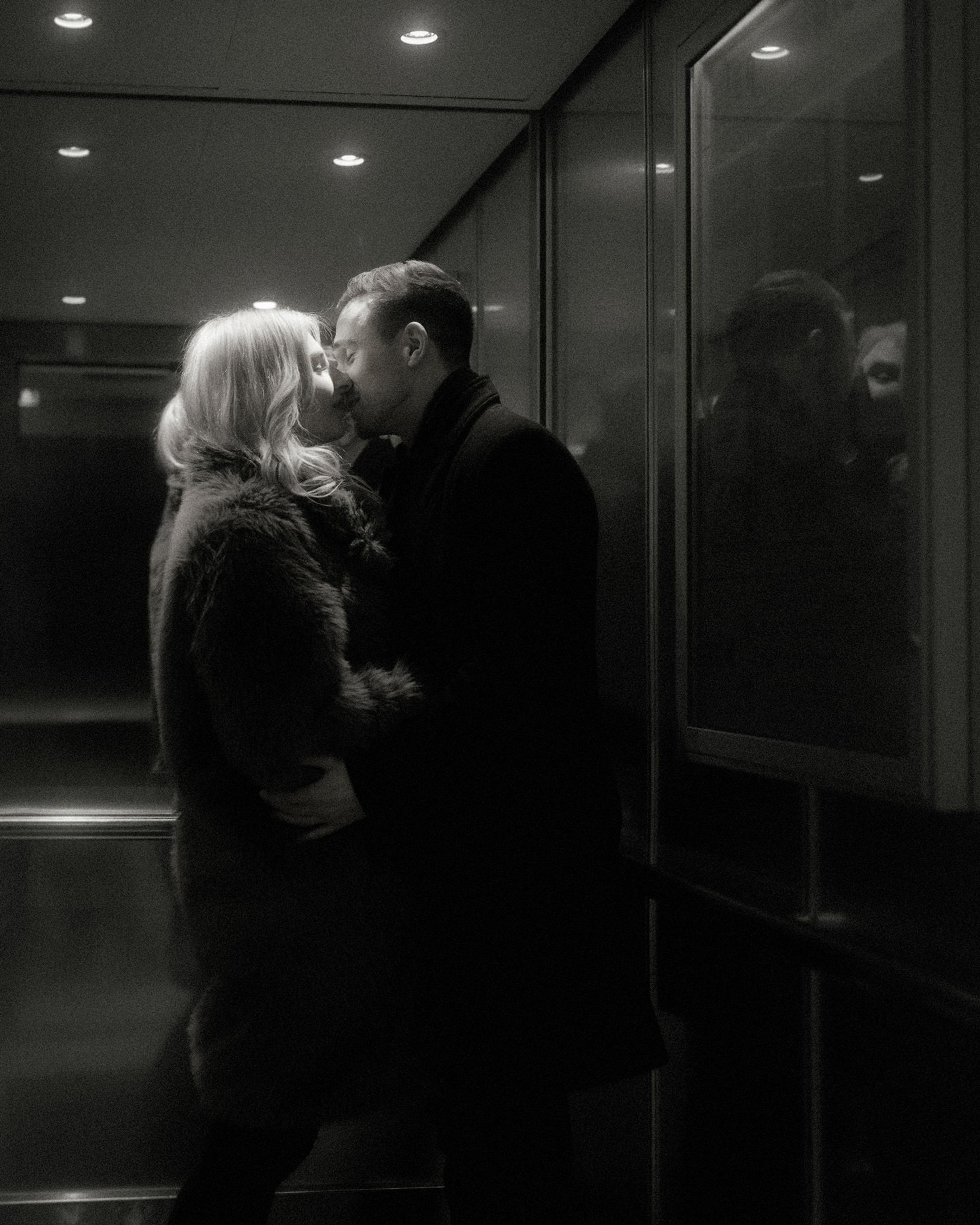 Lorelai and Steffen kiss inside a mirrored hotel lift in black and white.