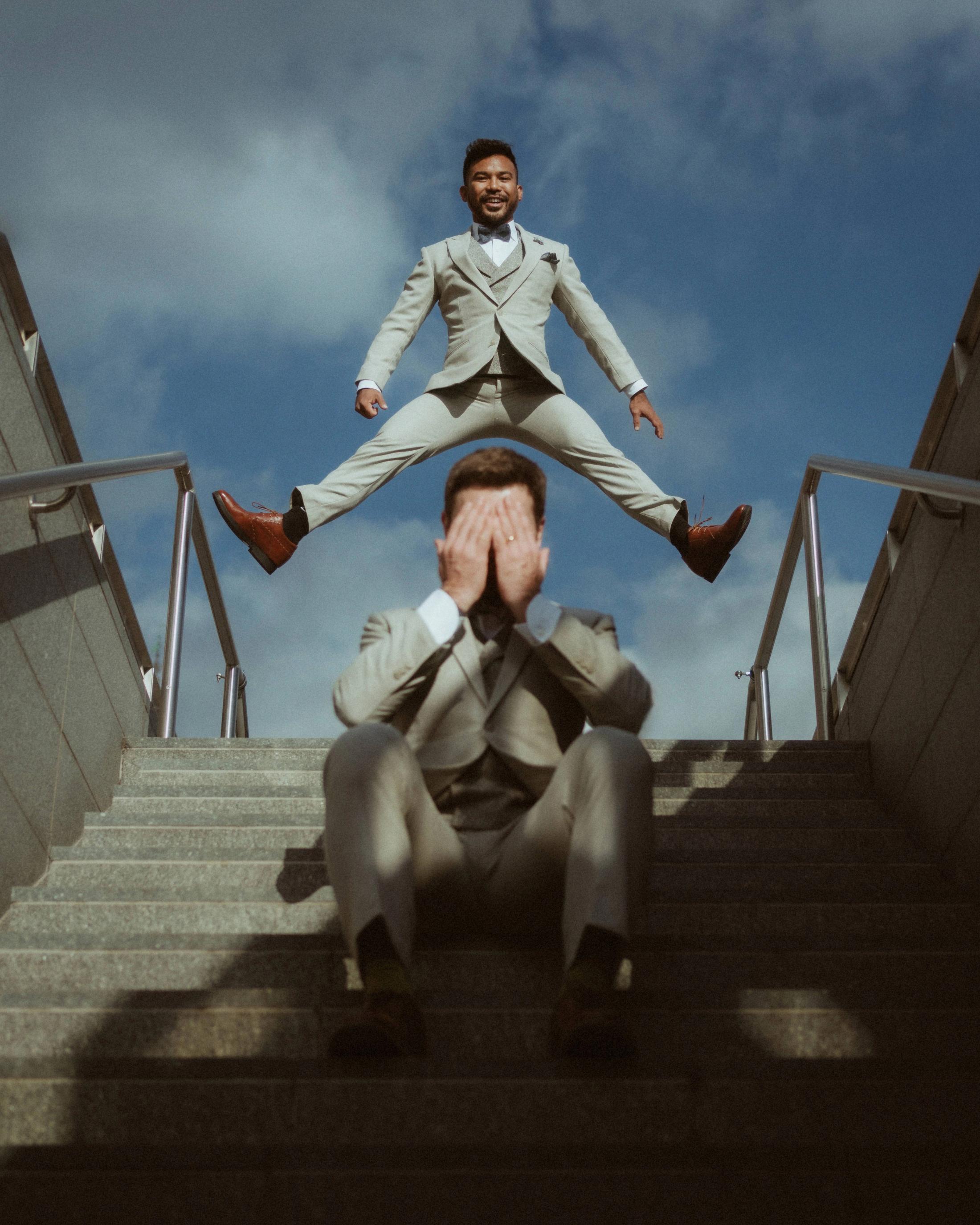 Playful vertical portrait of one partner standing above the other on an outdoor staircase.