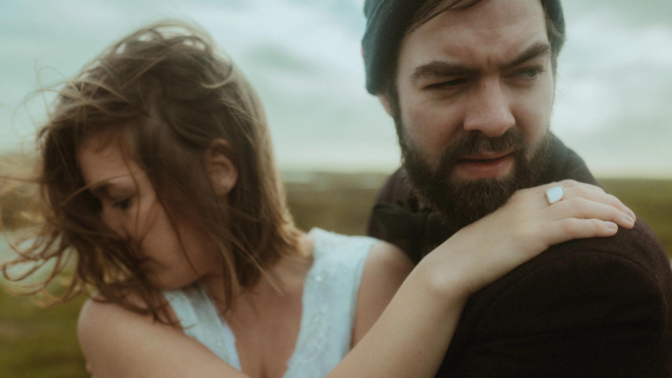 Anni holds Daniel's shoulder while they look in separate directions.