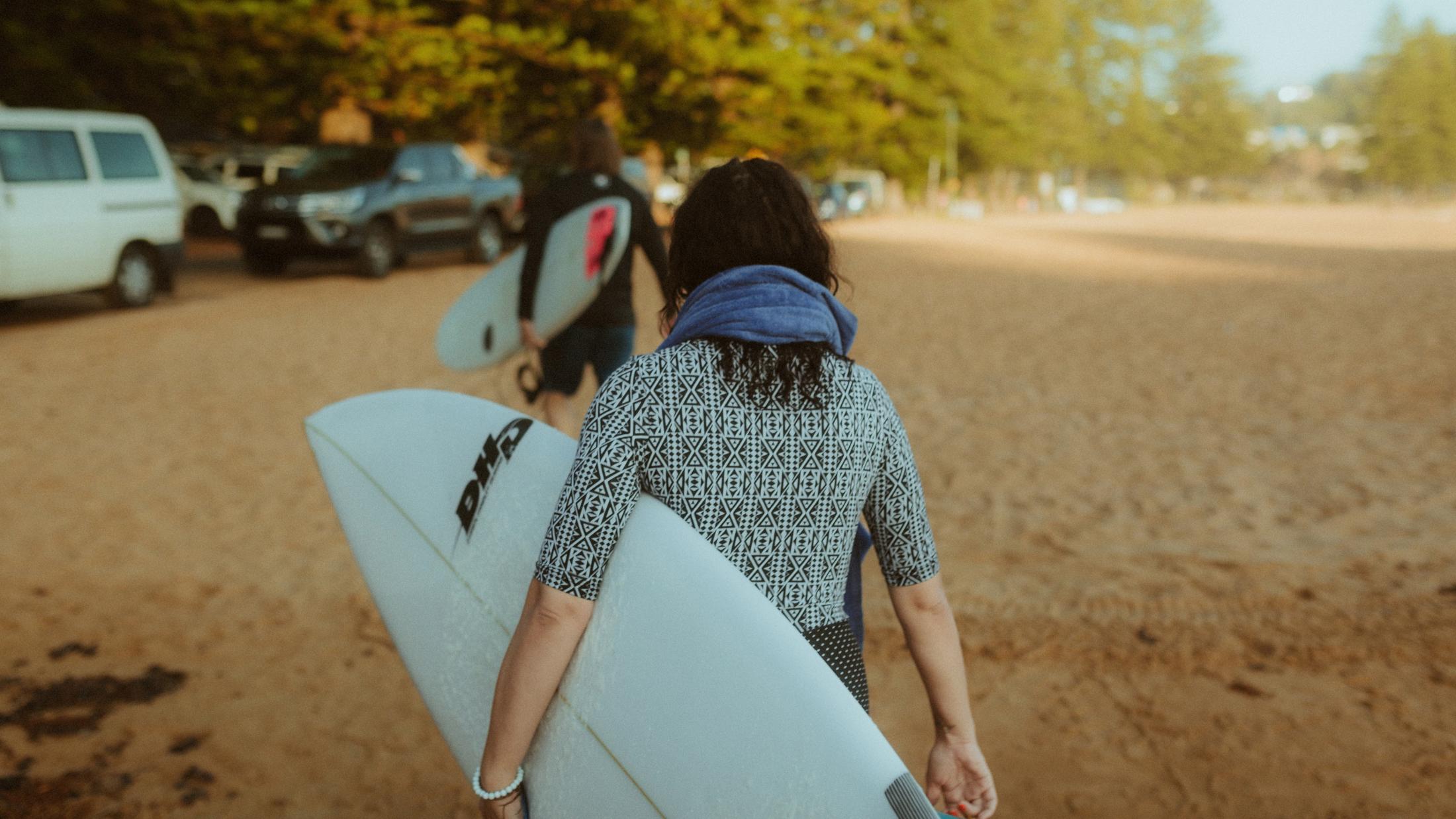 Petra carrying a white surfboard from the beach