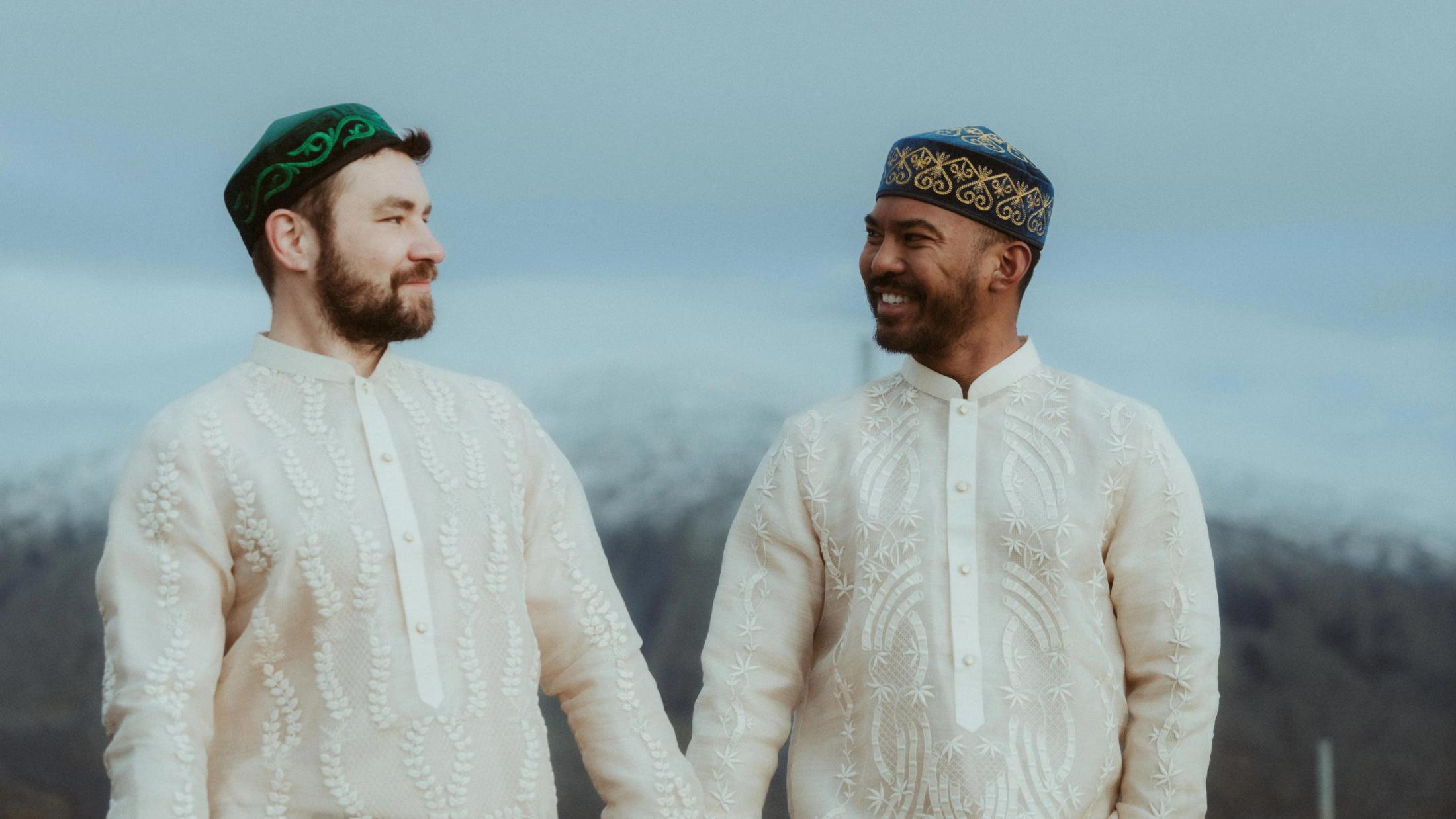 Kris und Ilya sehen sich in traditionellen Hemden vor dem offenen Himmel an.