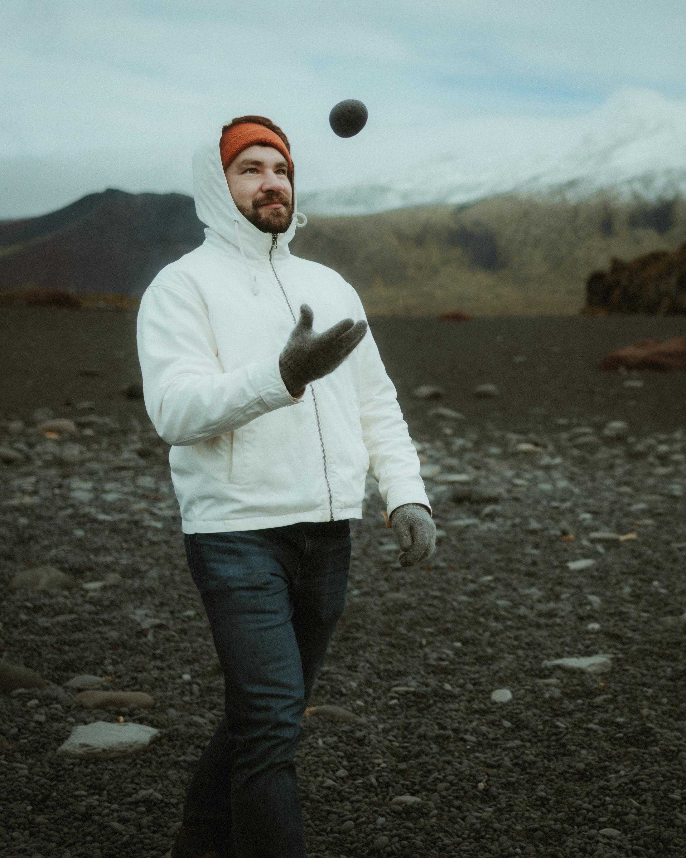 Kris wirft am schwarzen Strand einen dunklen Stein in die Luft.