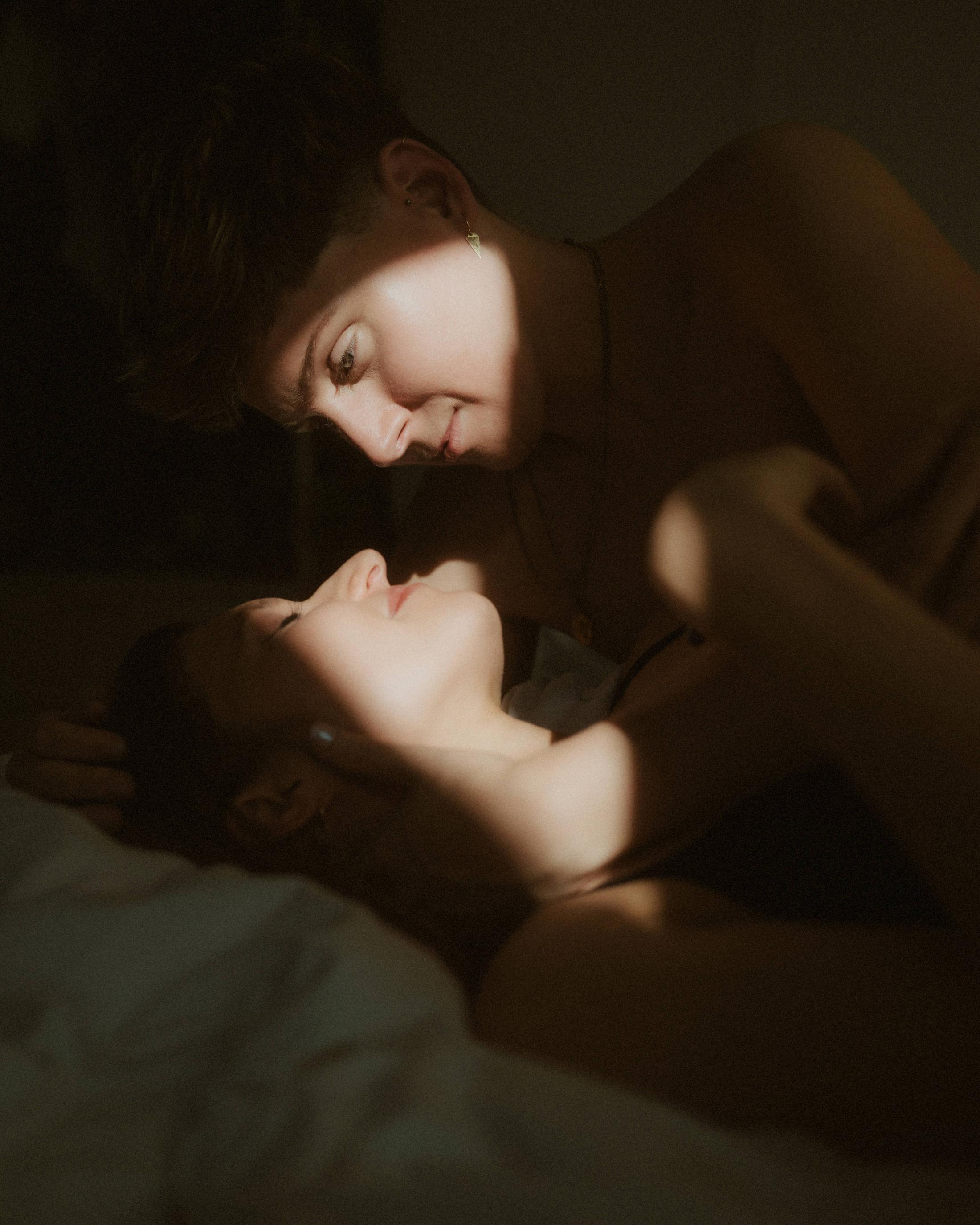 Noah and Michèle embracing in a narrow patch of dark amber light.