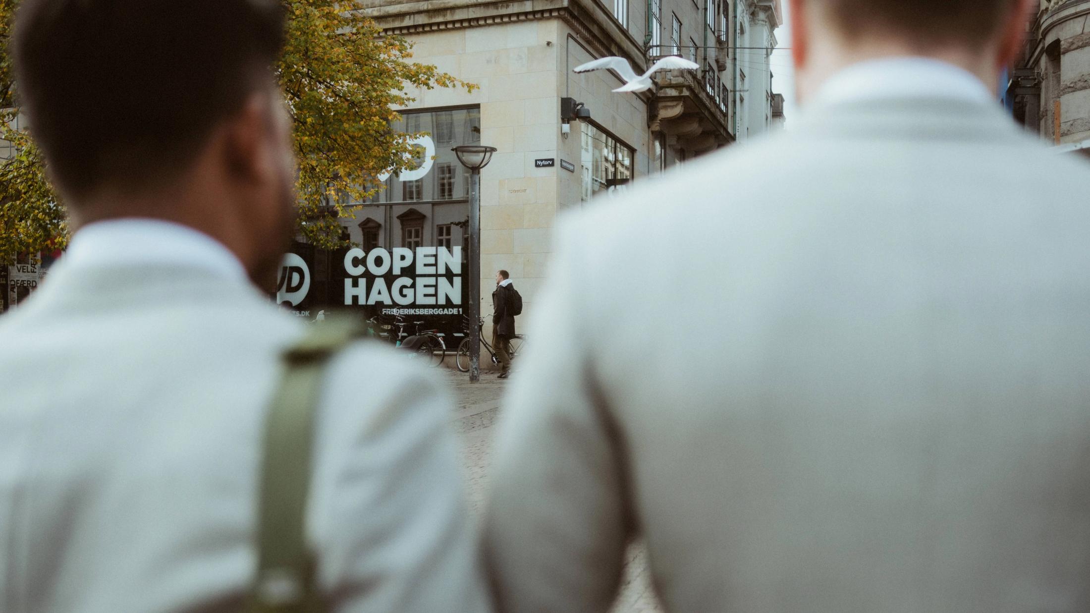 Kris and Ilya leave the hotel beneath a glass door marked Skt. Petri.