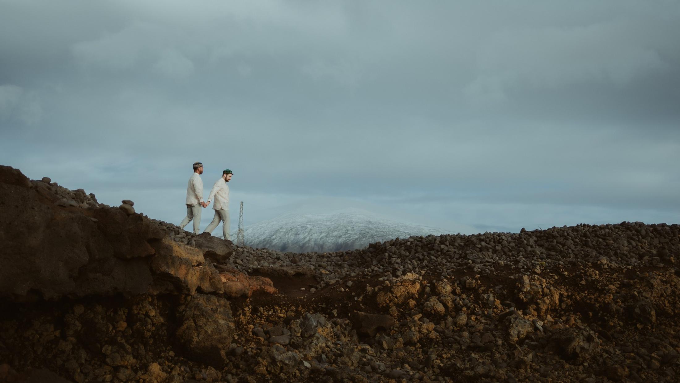Two people standing on a rocky ridge beneath a pale sky.
