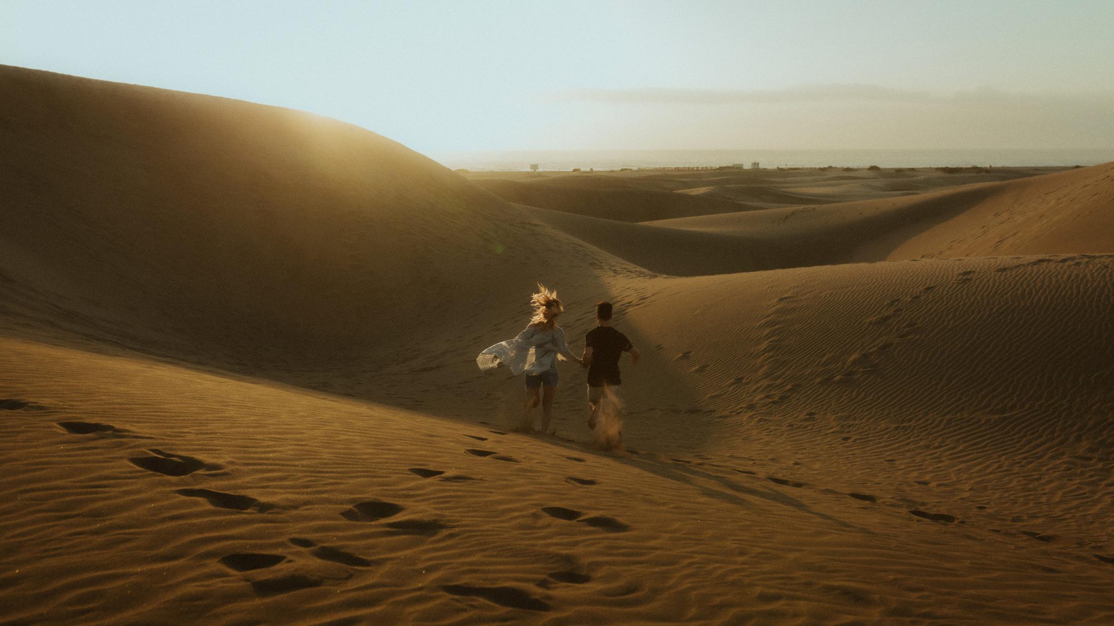 Katja and David running down a sandy slope in wide landscape.