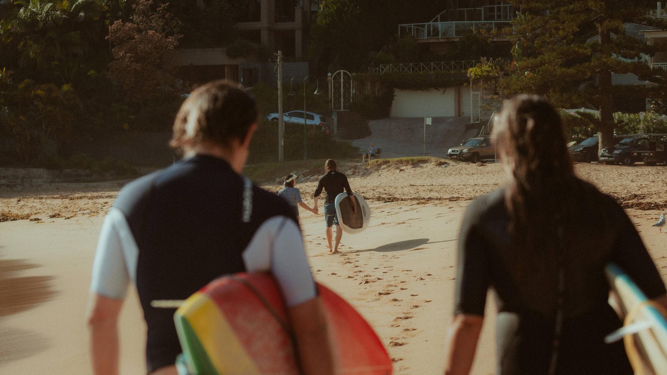 Witnesses with surfboards in the foreground as Petra and Roman walk away
