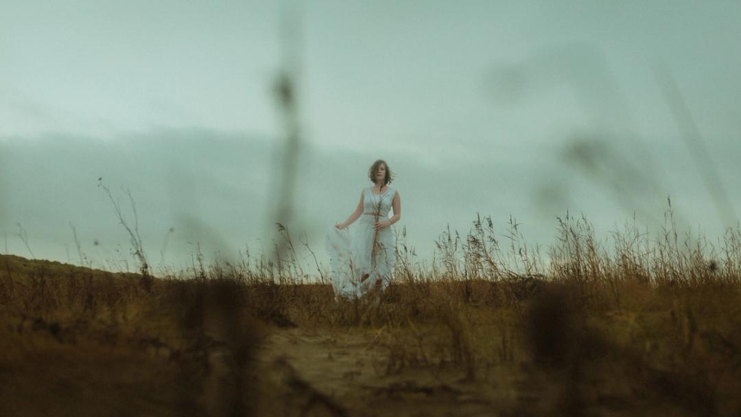 Anni stands small and alone beyond blurred dune grass.