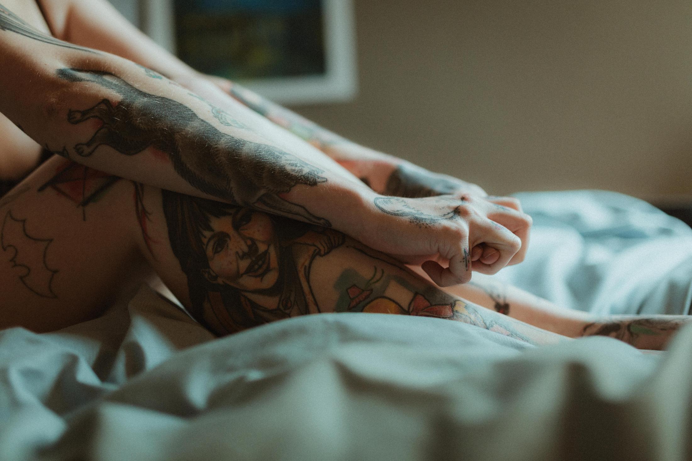 A close view of Anki’s tattooed hand, leg and torso on the bed.