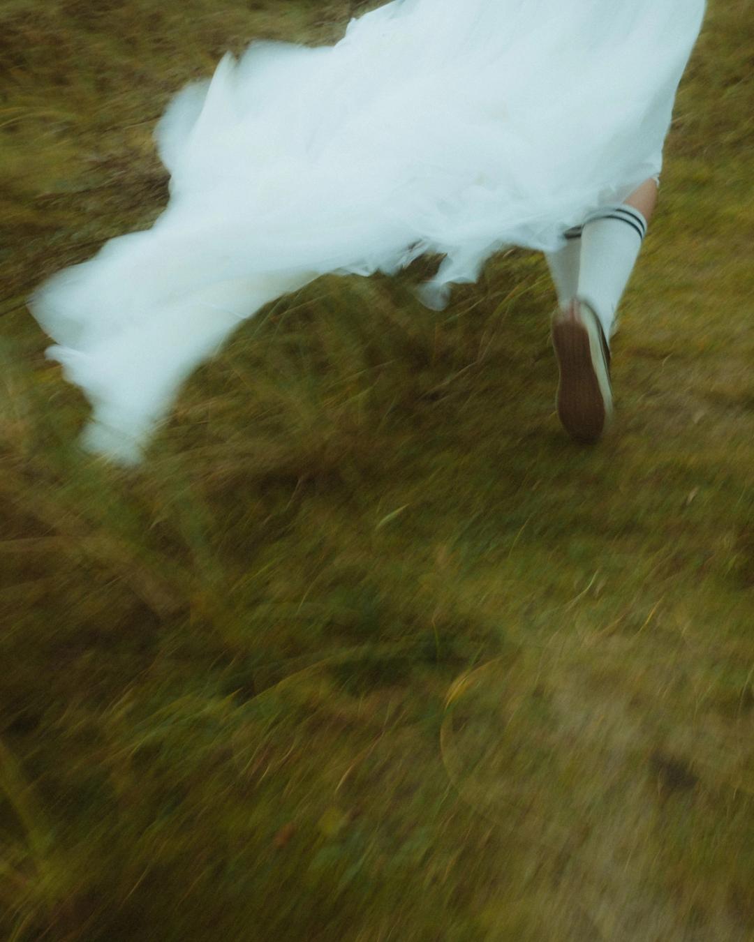 Anni's white skirt and legs blur as she runs across the grass.