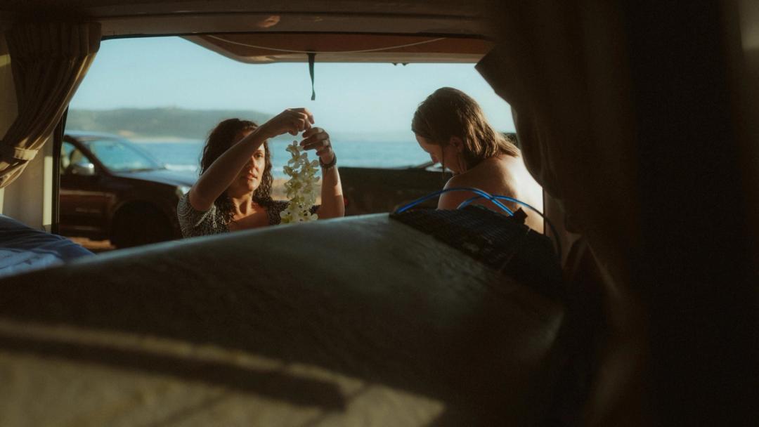 Petra and Roman prepare flowers by the open van, seen from the bed inside.