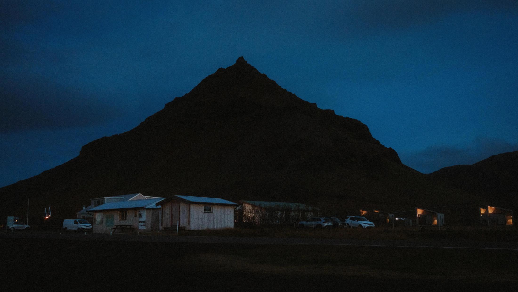 Kirkjufell erhebt sich im tiefblauen Licht vor Sonnenaufgang über kleinen Häusern.
