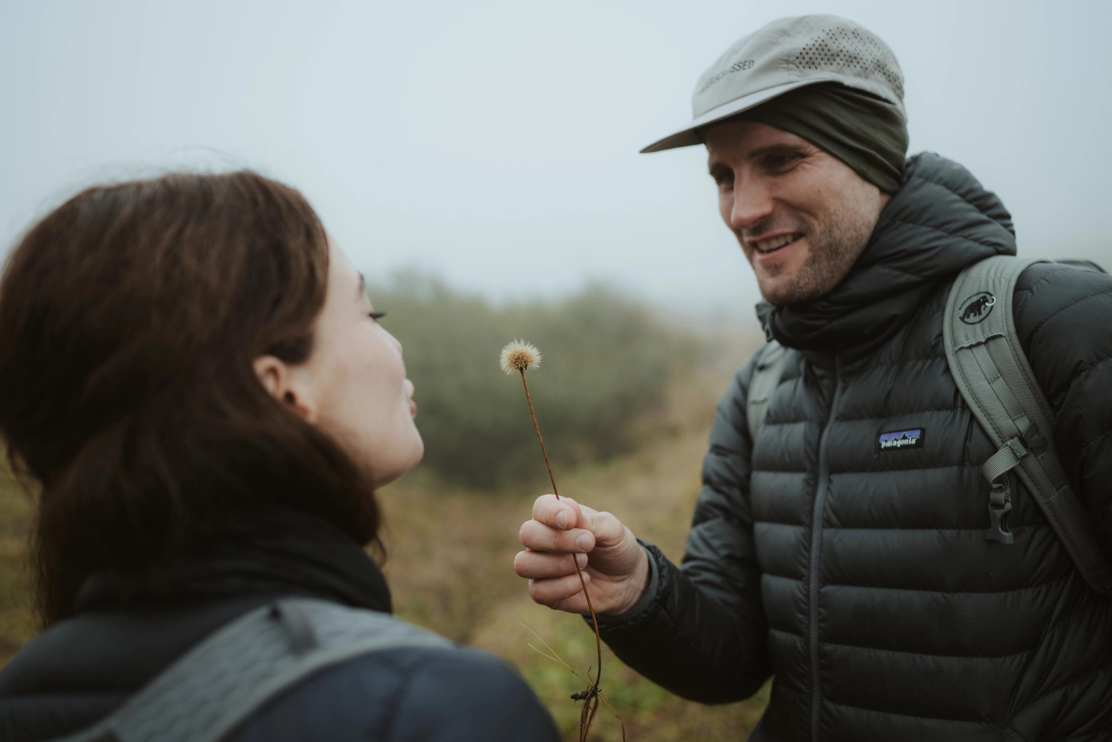 Jana holding a dandelion toward Steffen on the foggy trail.