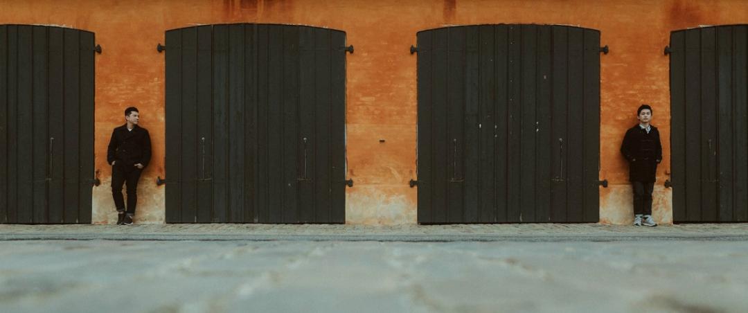 One of the grooms stands alone against an orange wall in Copenhagen.