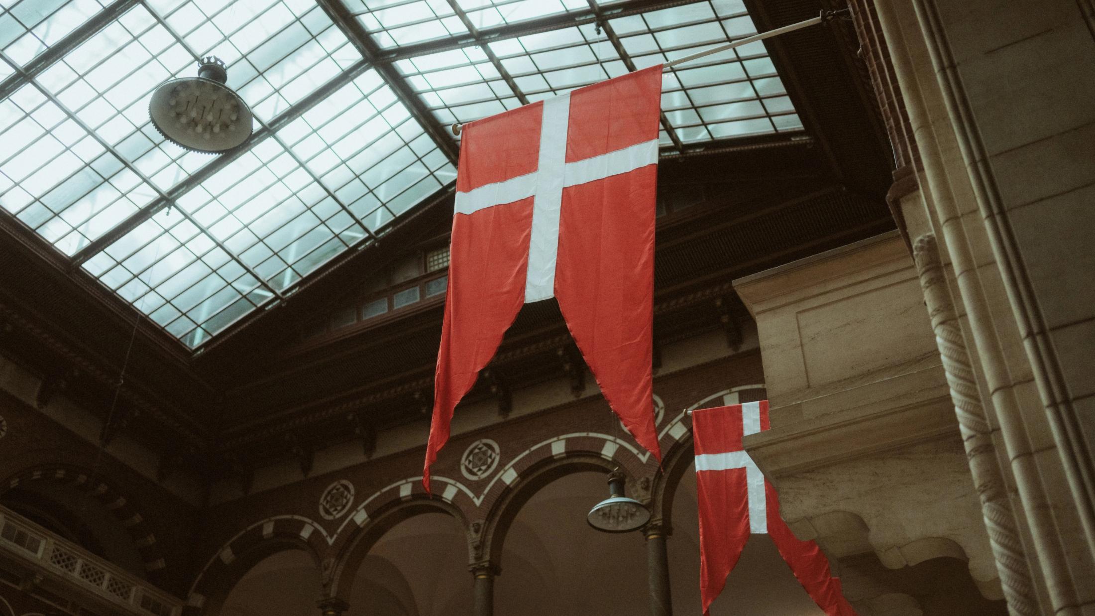 Danish flags hang beneath the glass roof inside Copenhagen City Hall.
