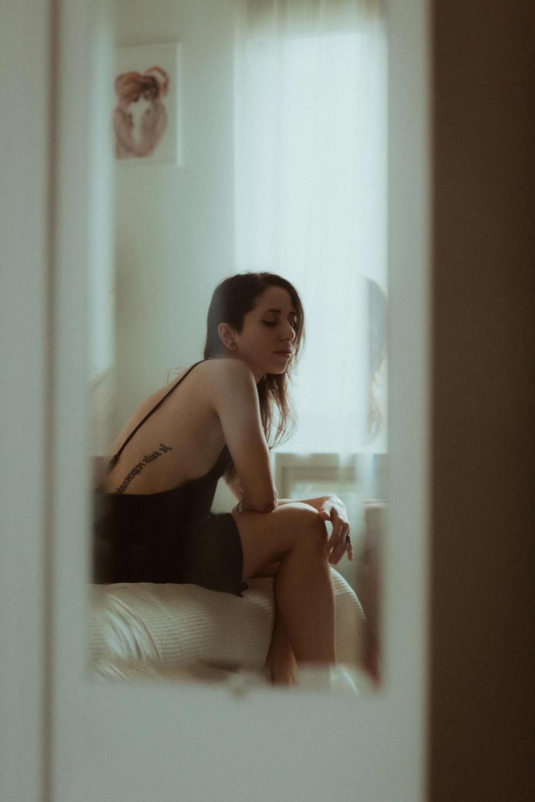 Maya sitting on her bed, photographed through the doorway.