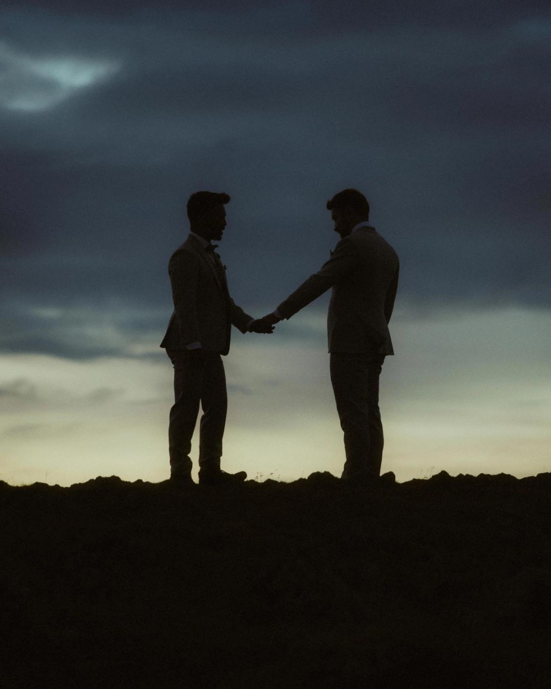 Kris und Ilya halten sich als Silhouetten unter einem stürmischen Morgenhimmel an den Händen.