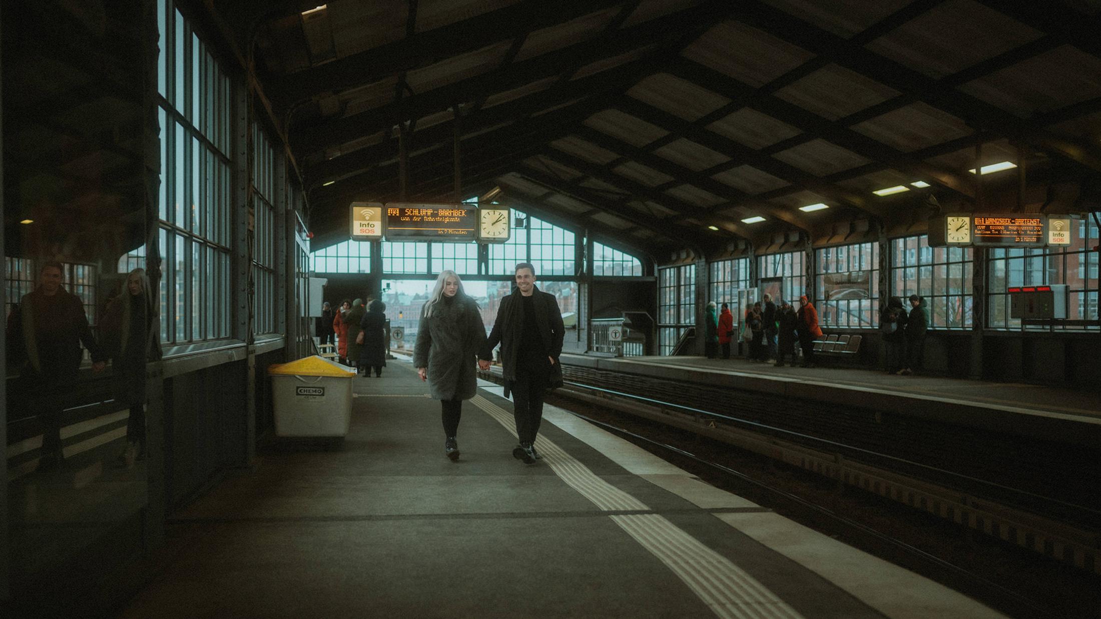 Lorelai and Steffen appear small beneath the wide roof of Baumwall station.