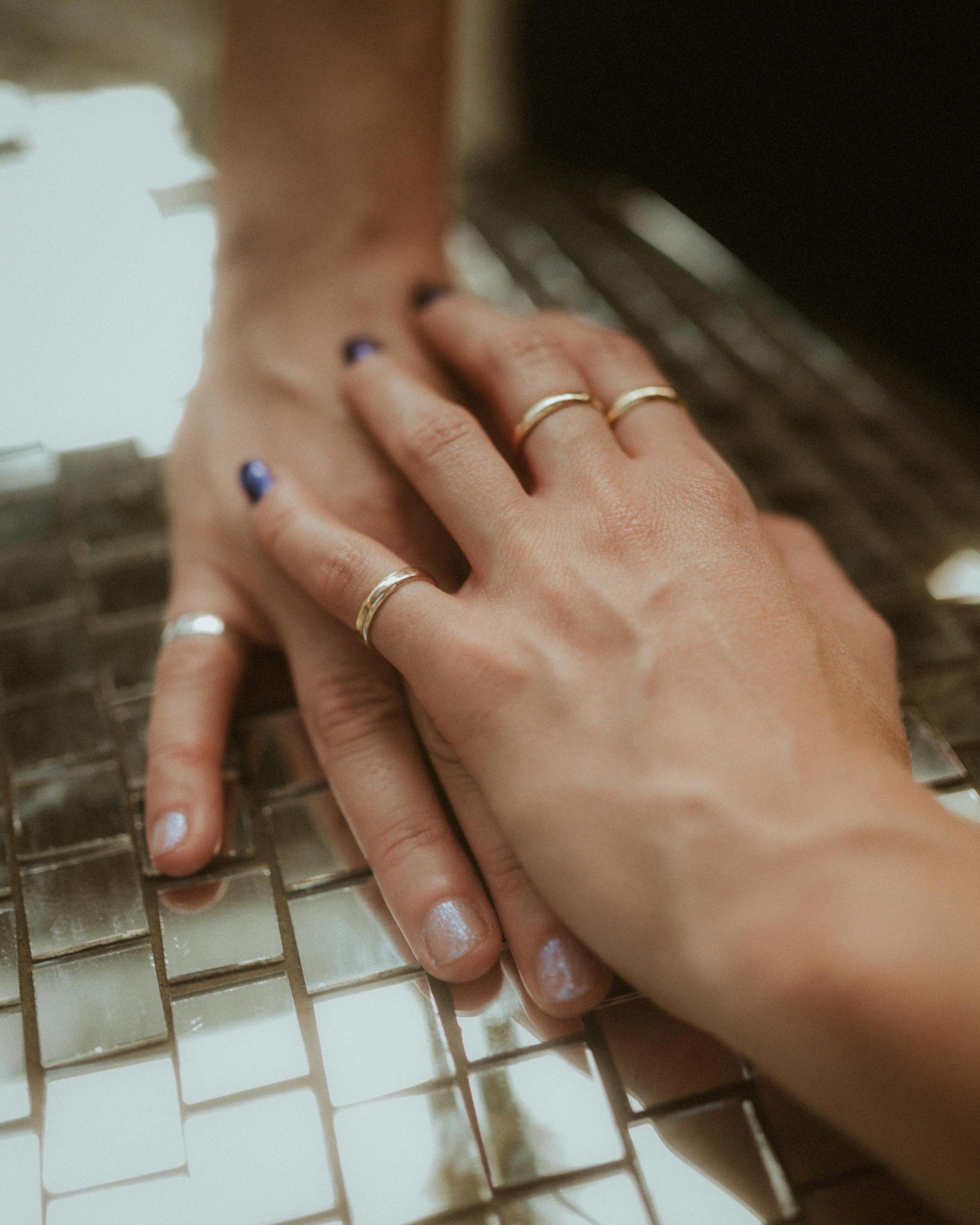 Noah and Michèle's ringed hands layered together on a mirrored surface.