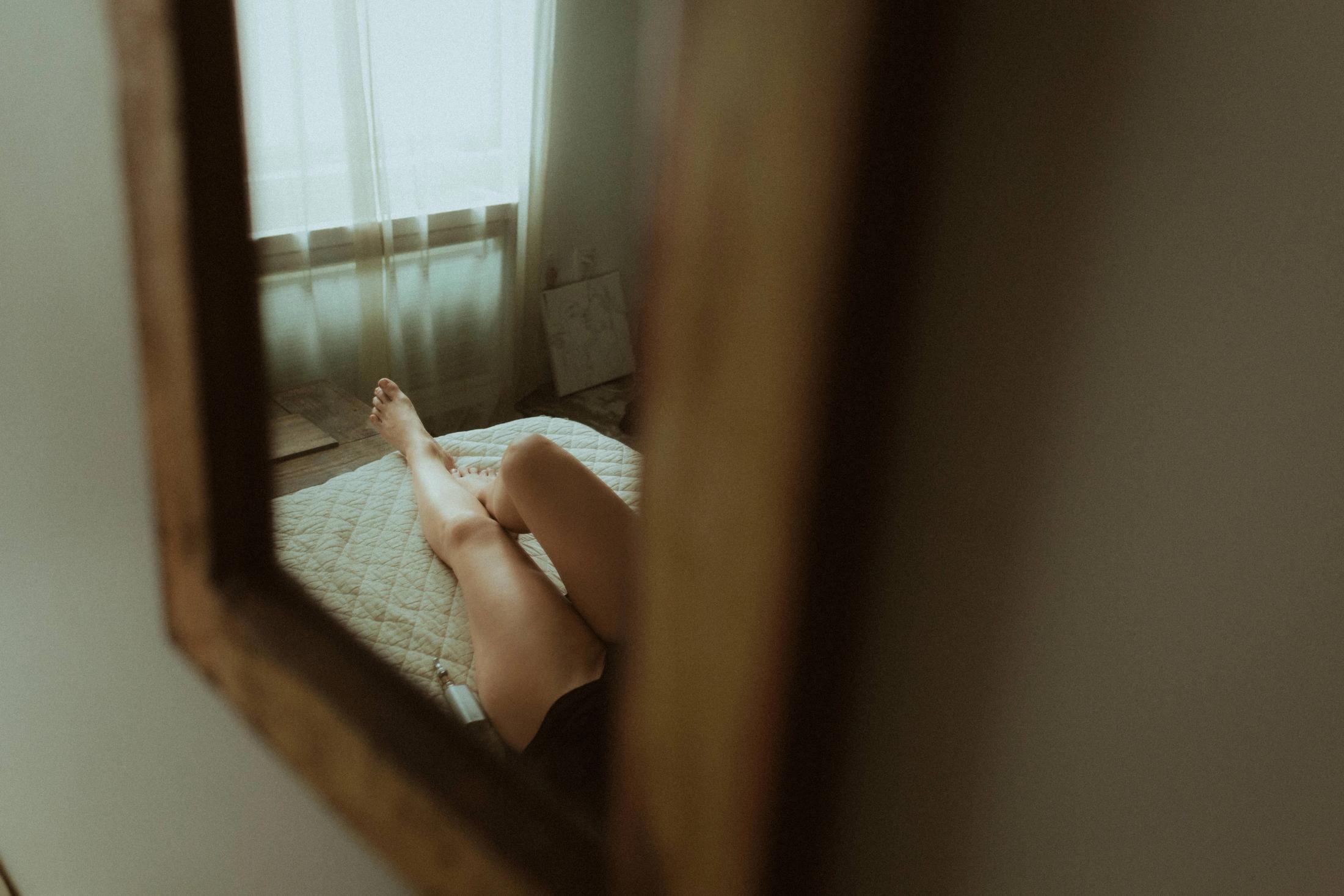 Maya reclining on the bed, seen through a dark wooden frame.