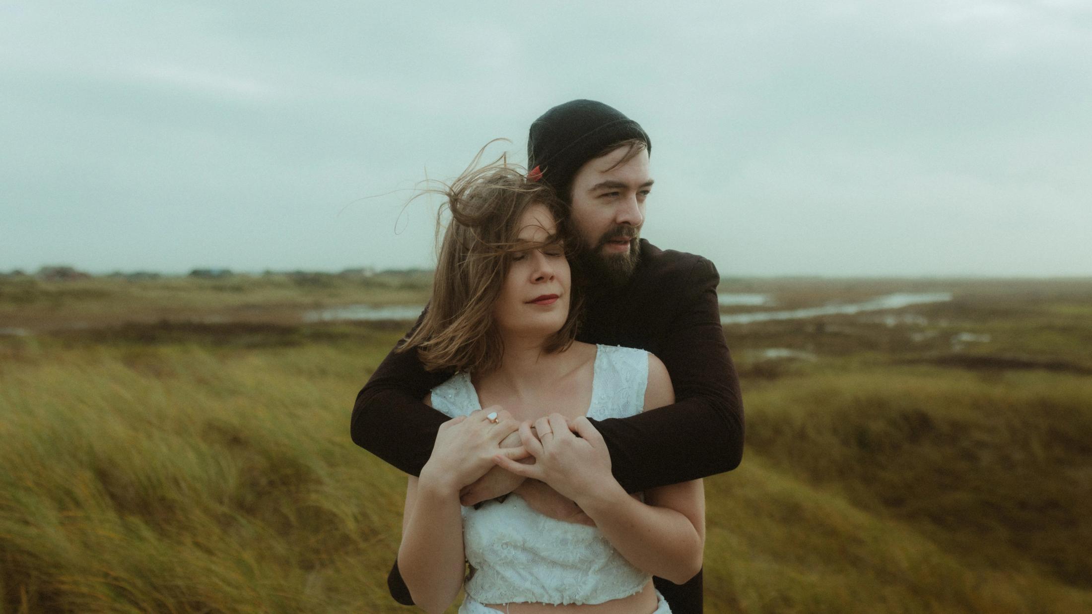 Daniel wraps his arms around Anni in the windswept marshland.