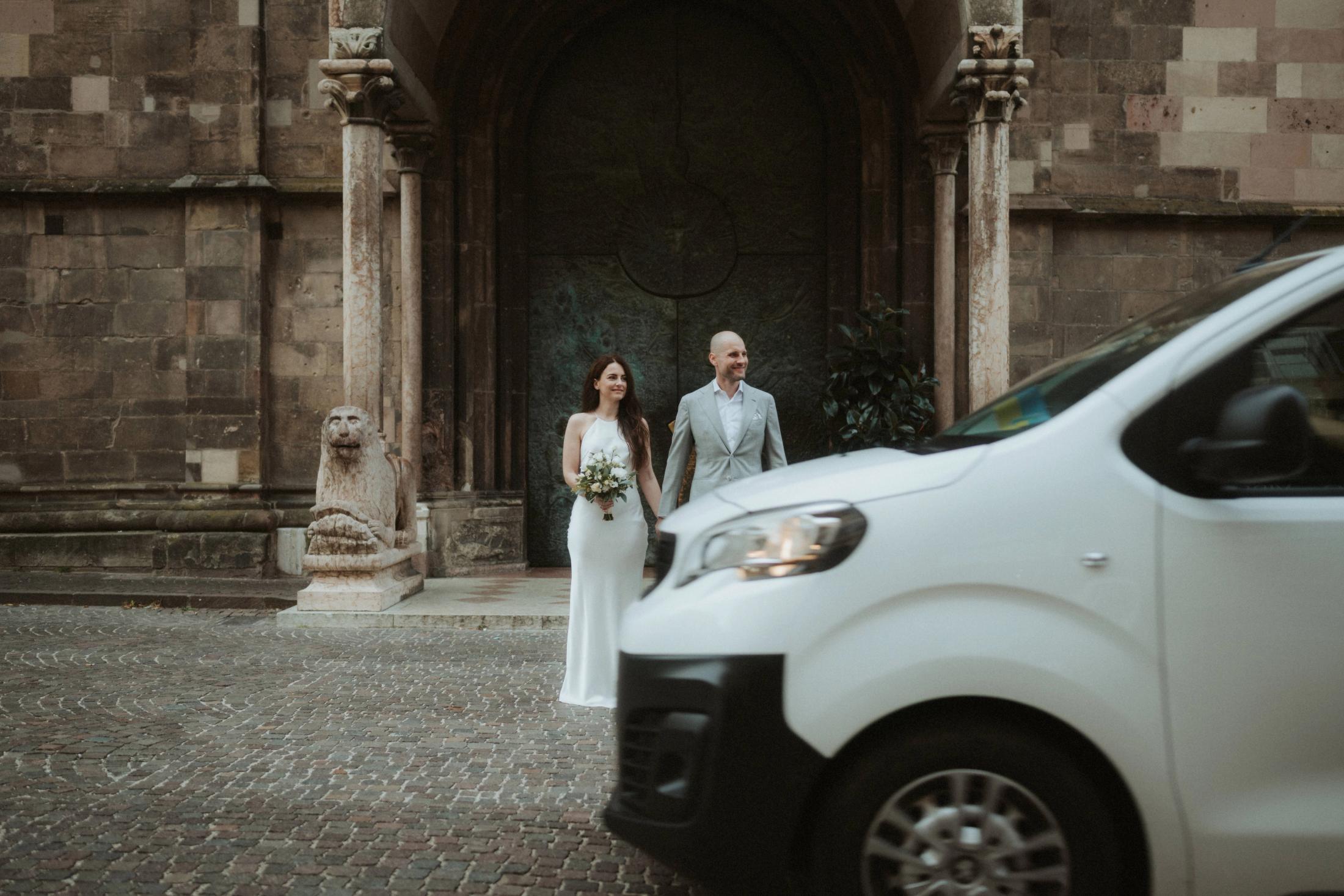 A delivery van passing between the camera and Jana and Steffen outside a church.