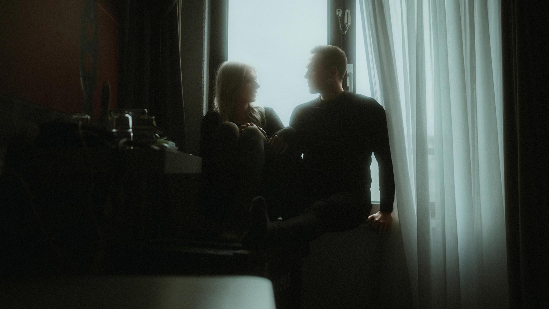 Lorelai and Steffen sit in silhouette beside a bright hotel window in Hamburg.