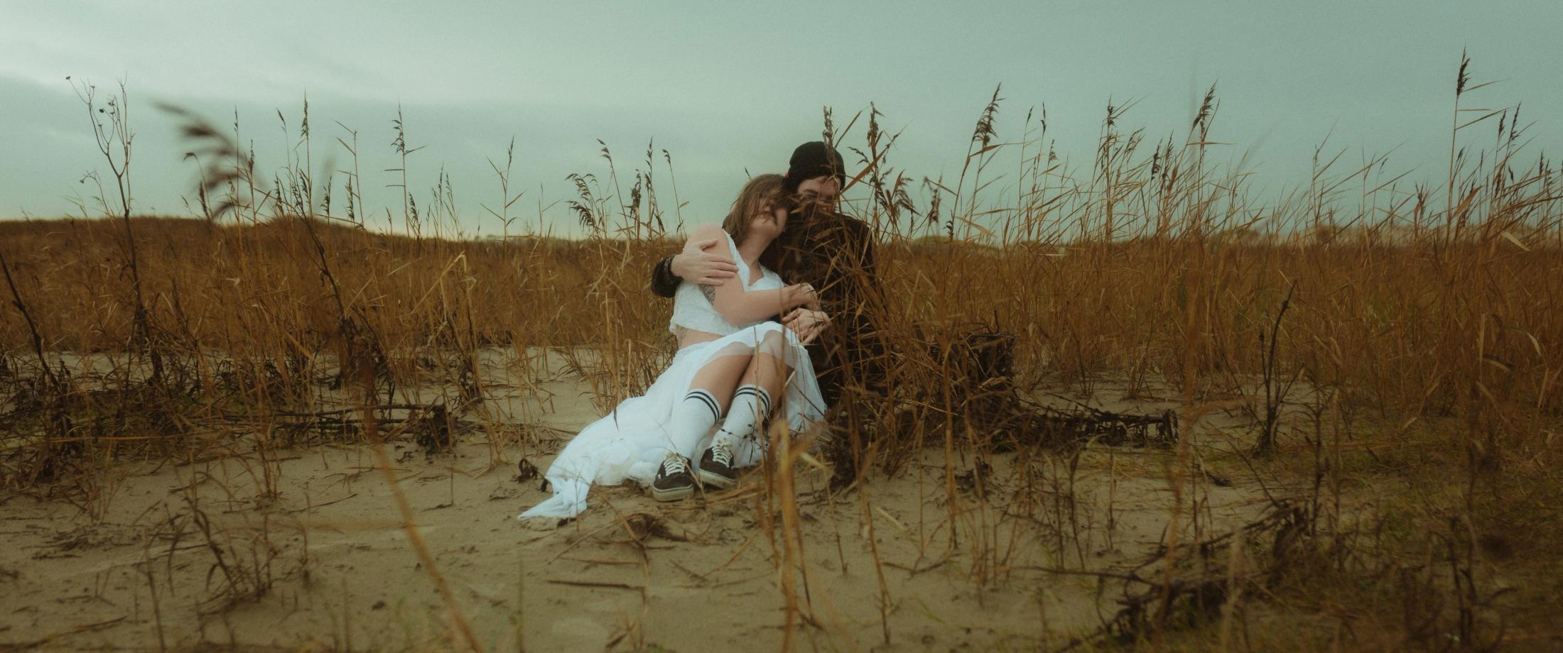 Wide view of the couple sitting low among tall brown reeds.