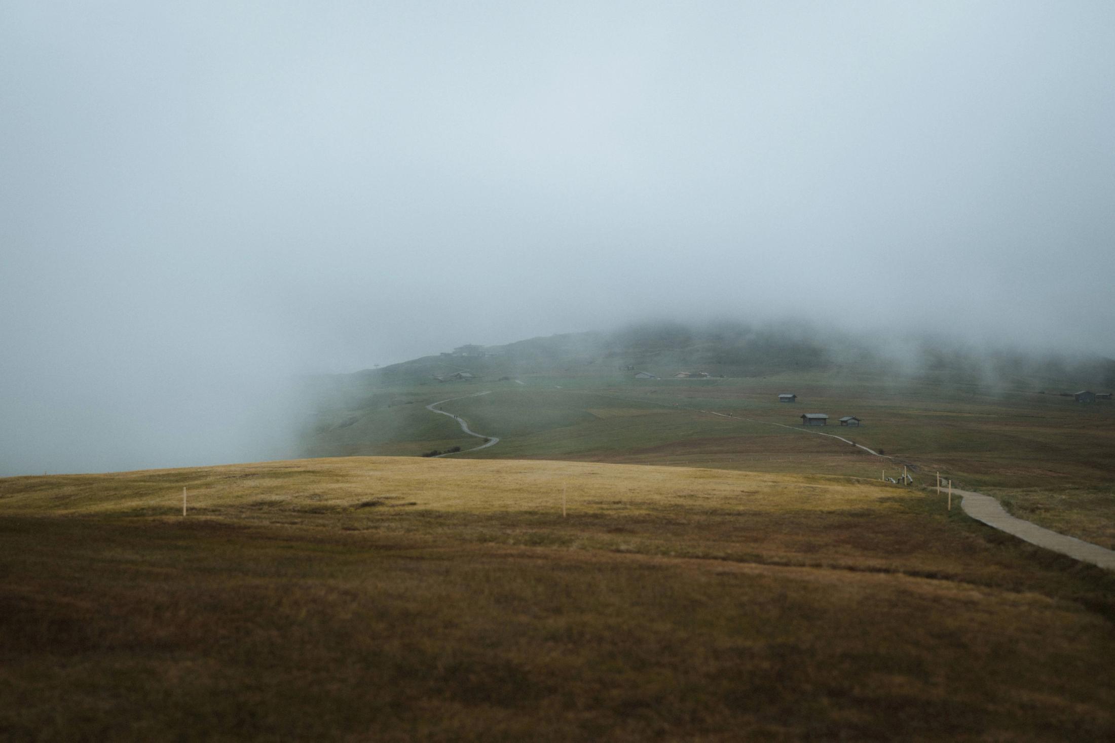 An empty mountain path disappearing into thick white fog.
