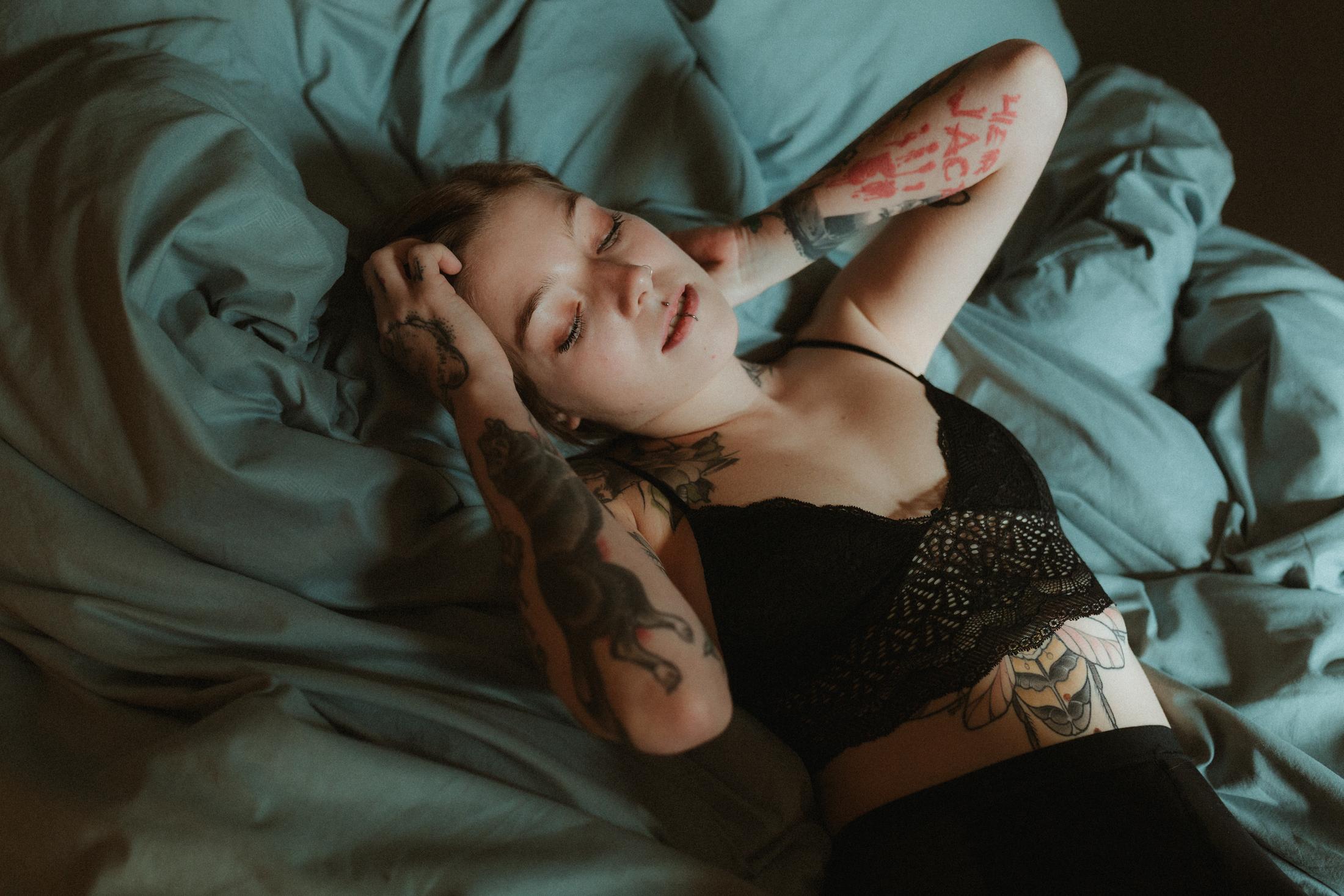 Anki lies curled on the bed, her tattooed back turned upward.