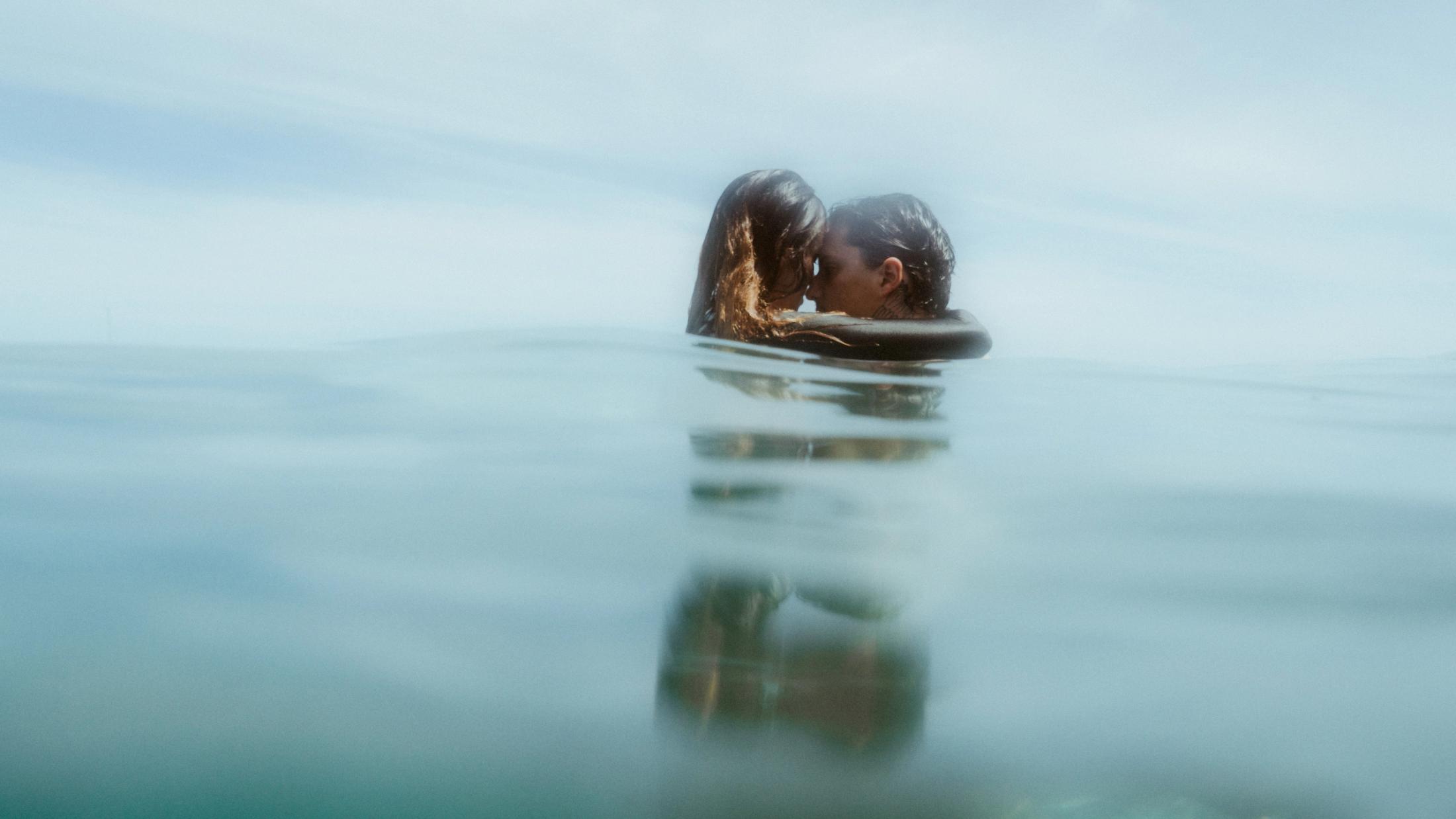 Angela und Ivan berühren sich mit der Stirn, stehen im flachen Wasser.