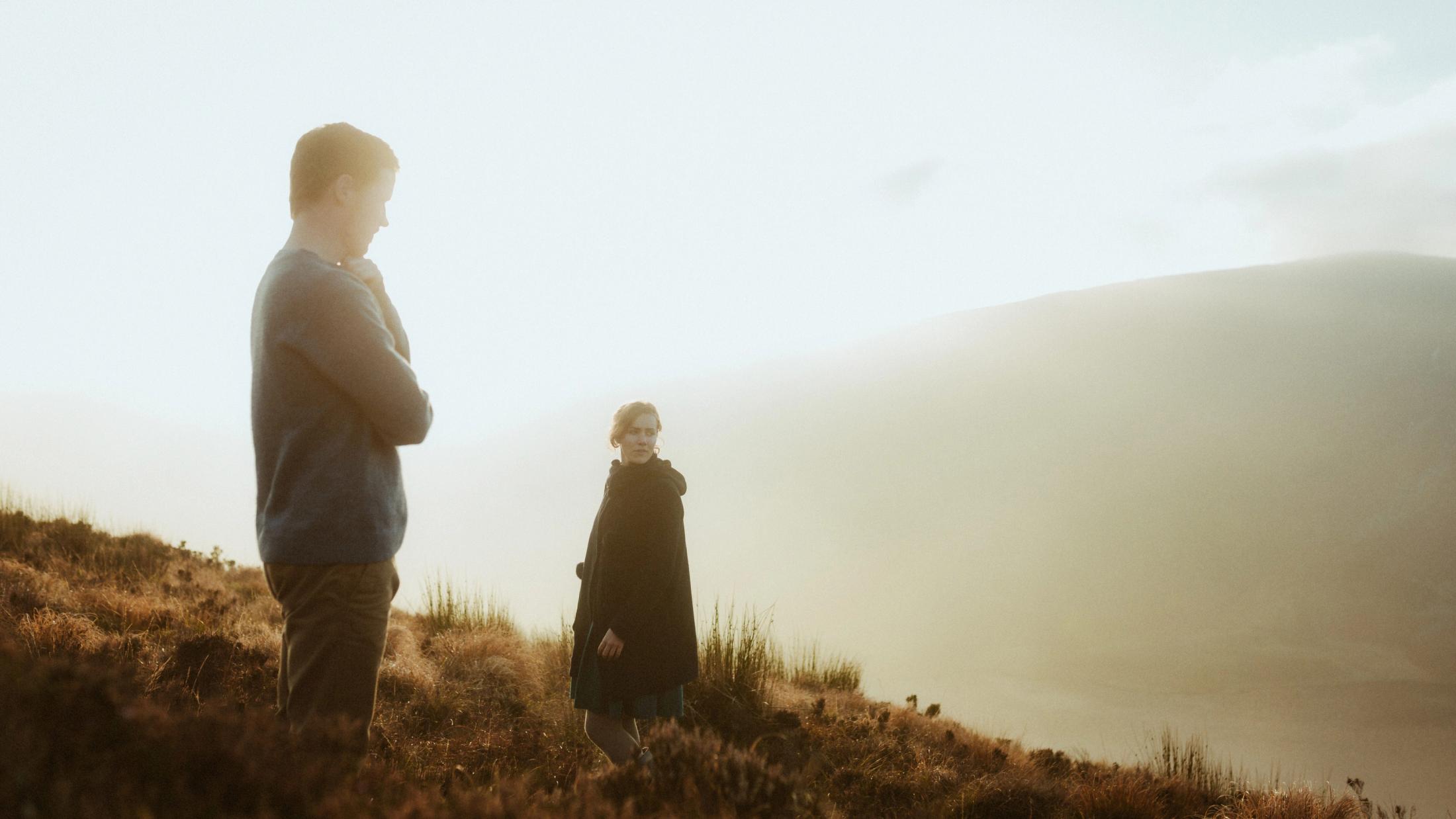 Jule und Rory stehen mit Abstand im warmen Abendlicht an einem Hang und sehen sich an.