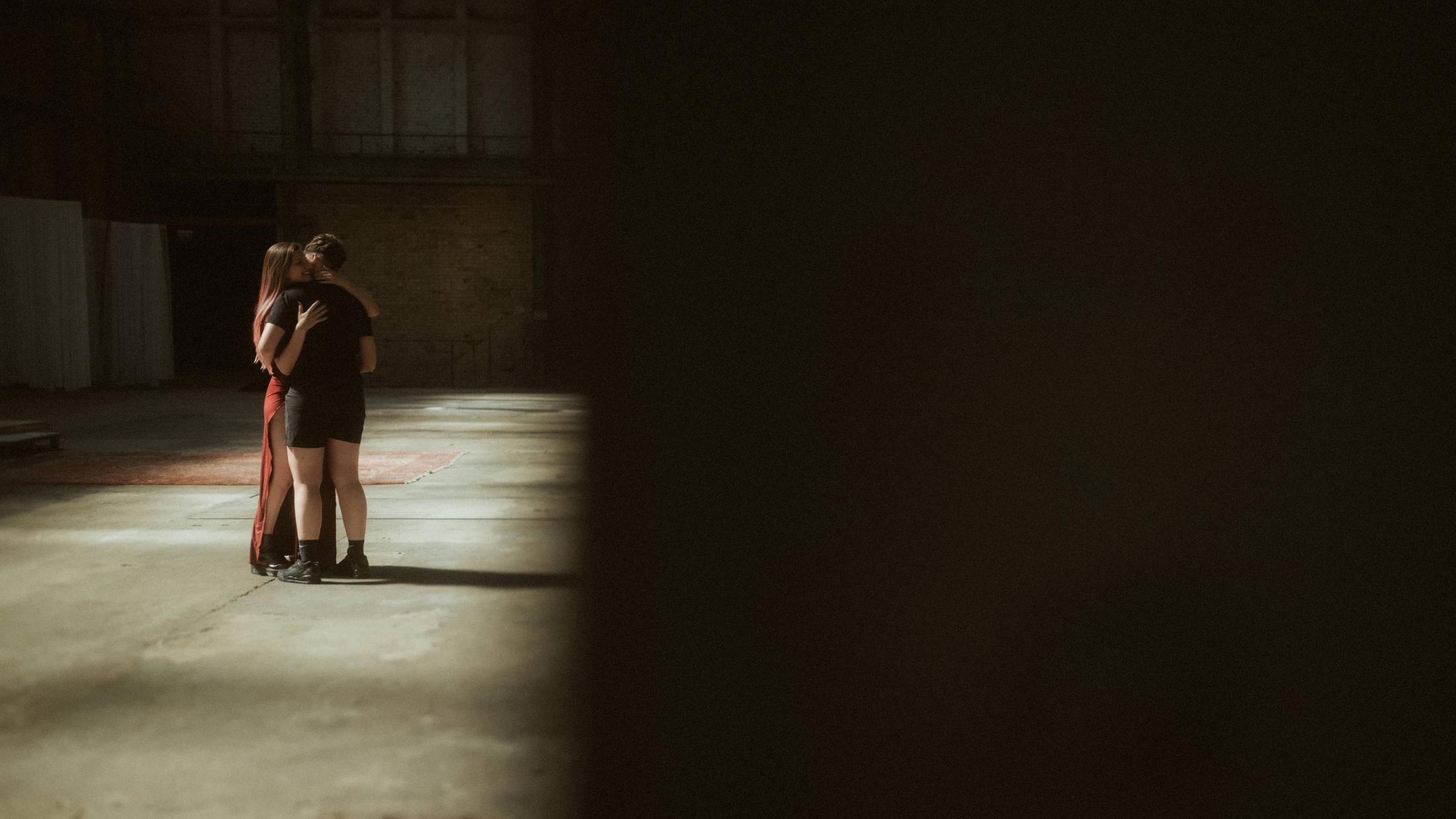 Noah and Michèle facing each other and holding hands in the industrial hall.