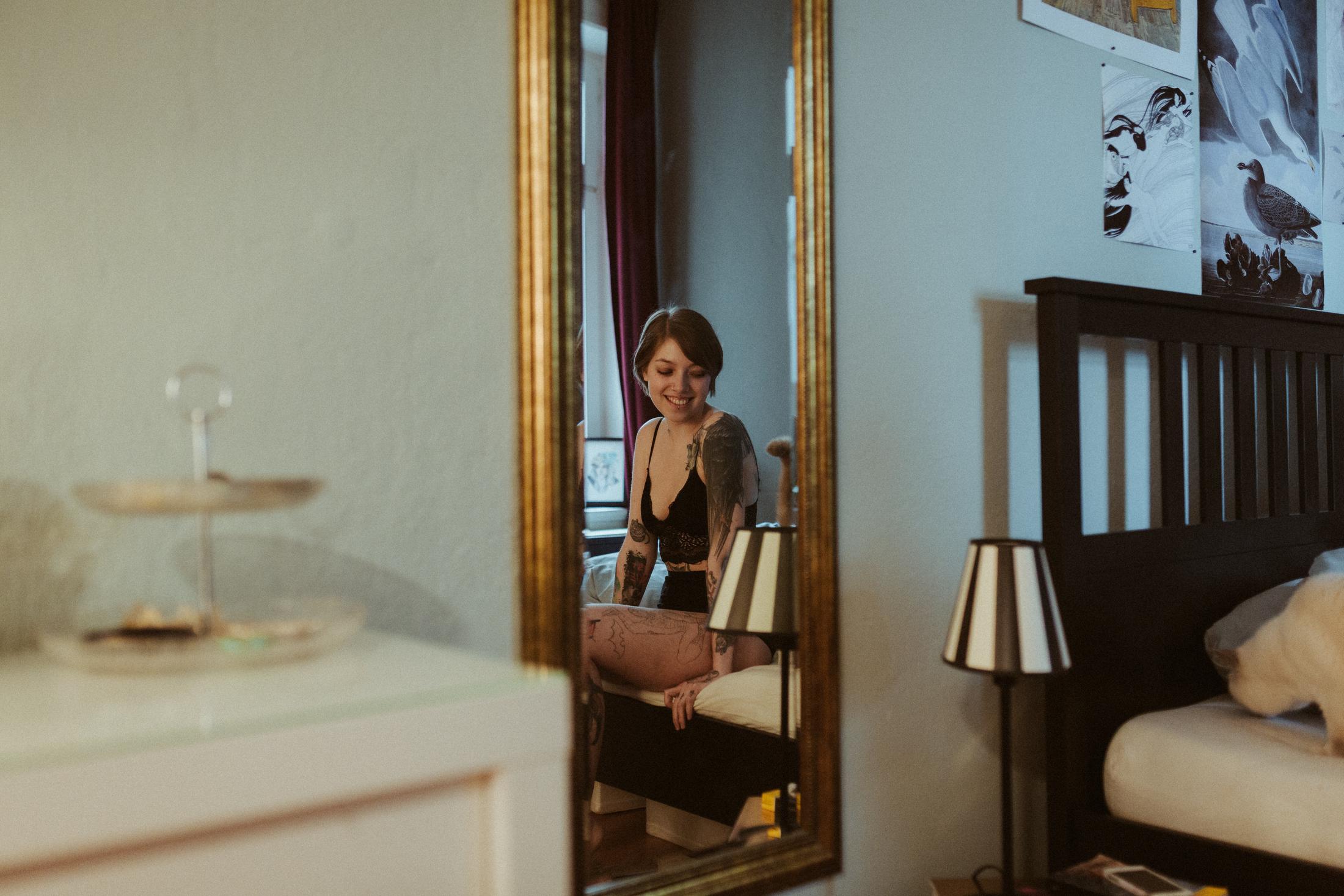 Anki sits in a bedroom, seen through a doorway and mirror.