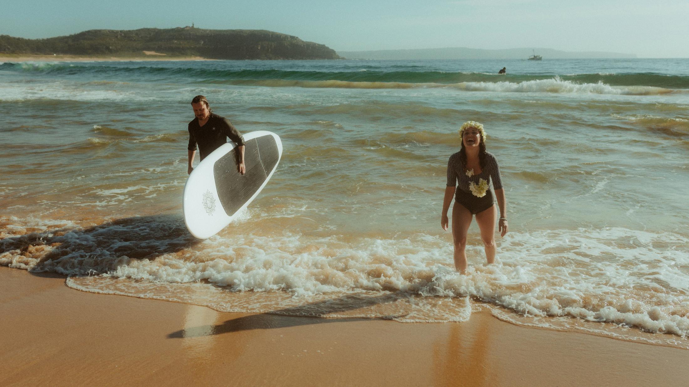 Petra and Roman walking out of the surf carrying a white board