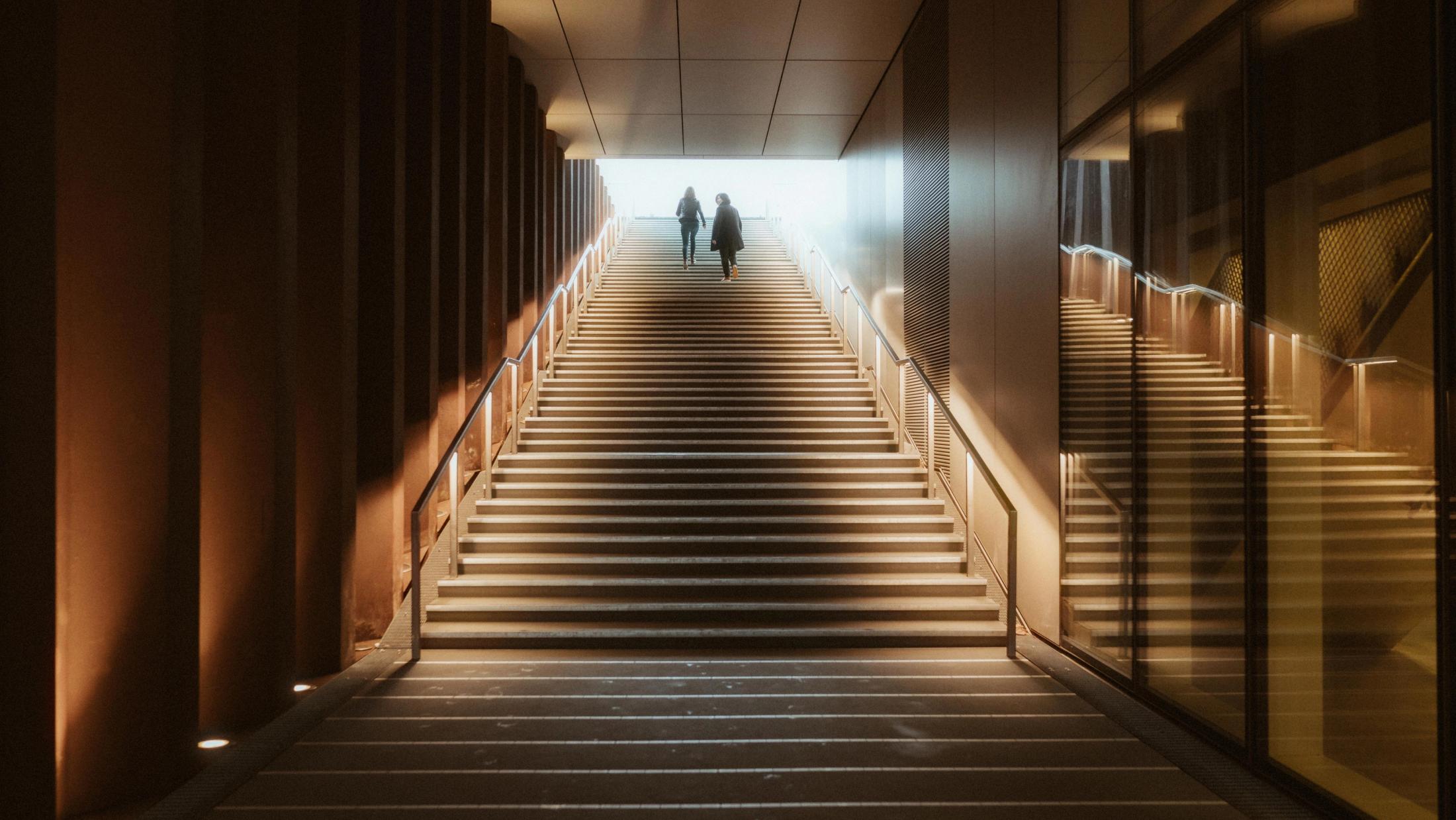 Ari and Pia walking up illuminated stairs toward the light