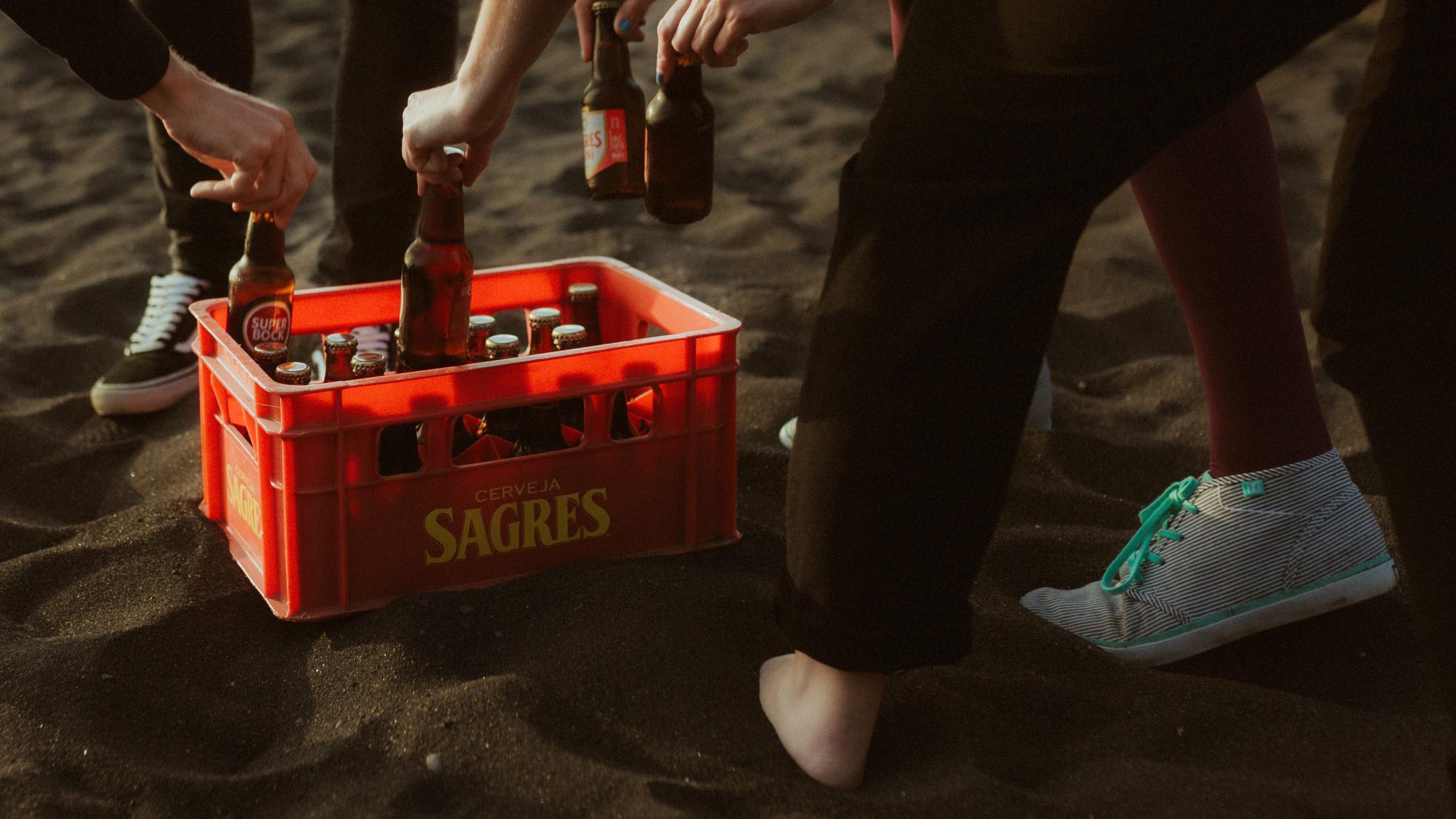Hands reach into a red beer crate during the gathering on the beach.