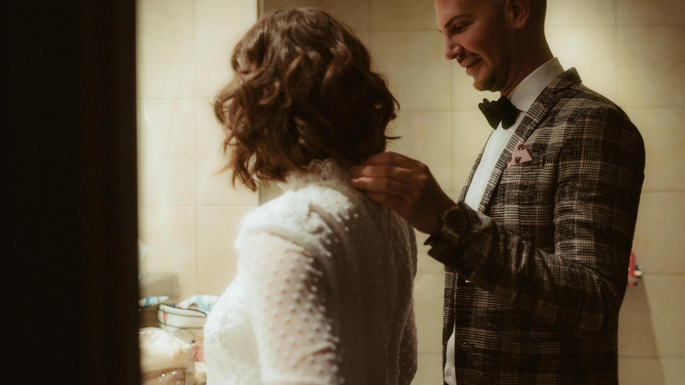 Pia fastening the lace collar of Ari's wedding top