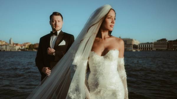 Cinematic waterfront portrait with the bride in a flowing veil and her partner standing behind her.