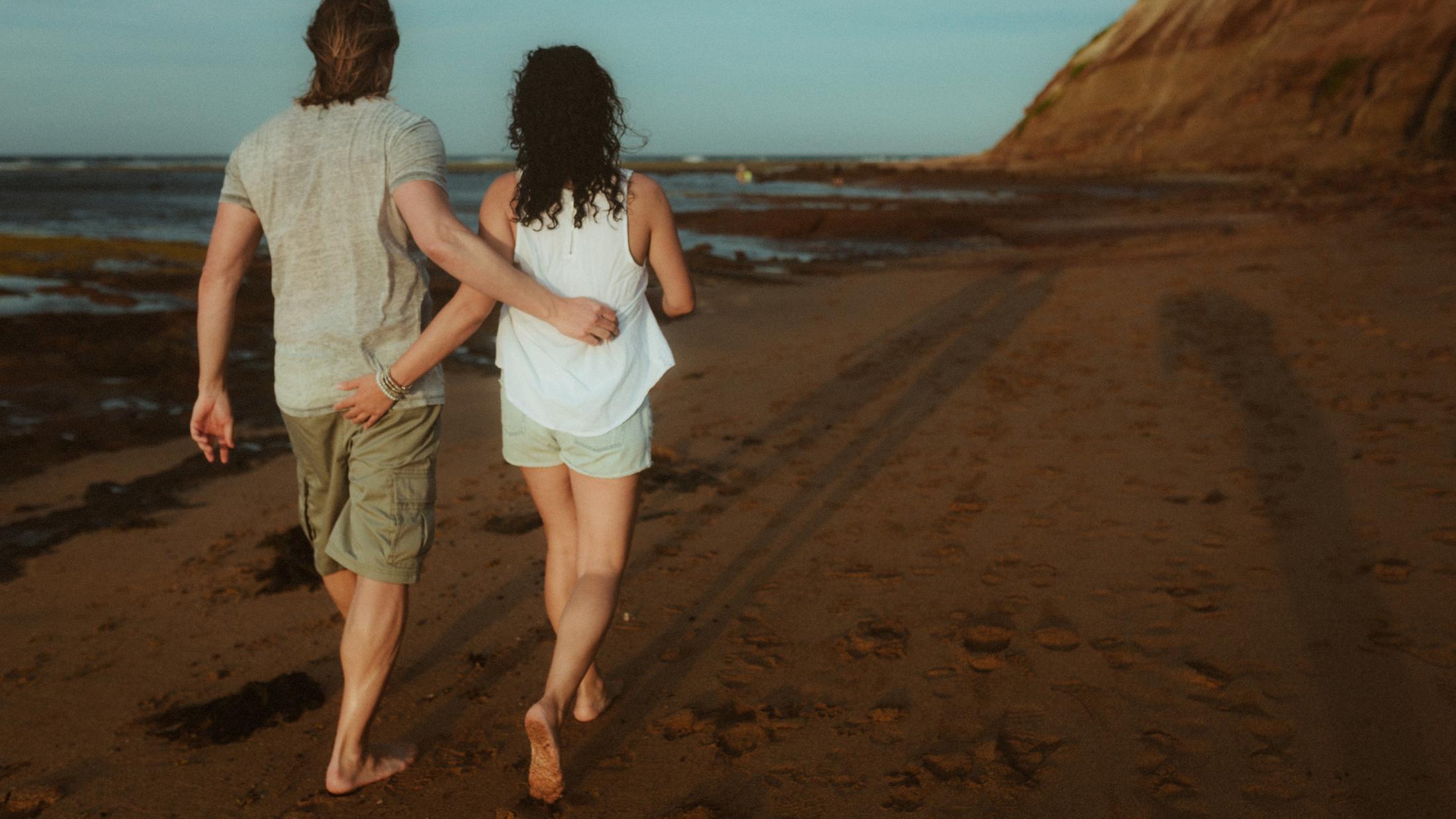 Petra and Roman walking barefoot along the beach with their arms around each other