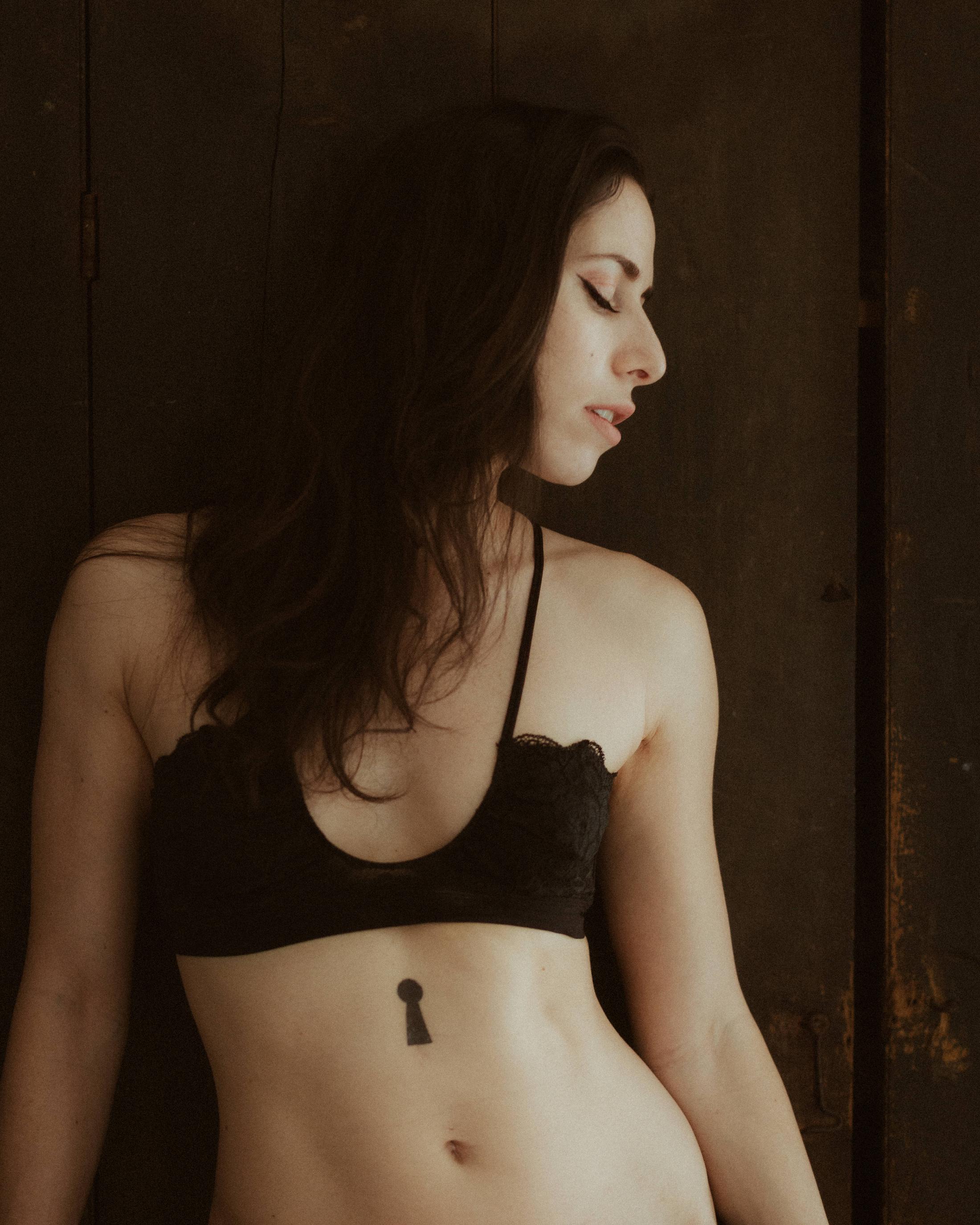 Maya standing in black underwear against dark wooden doors.