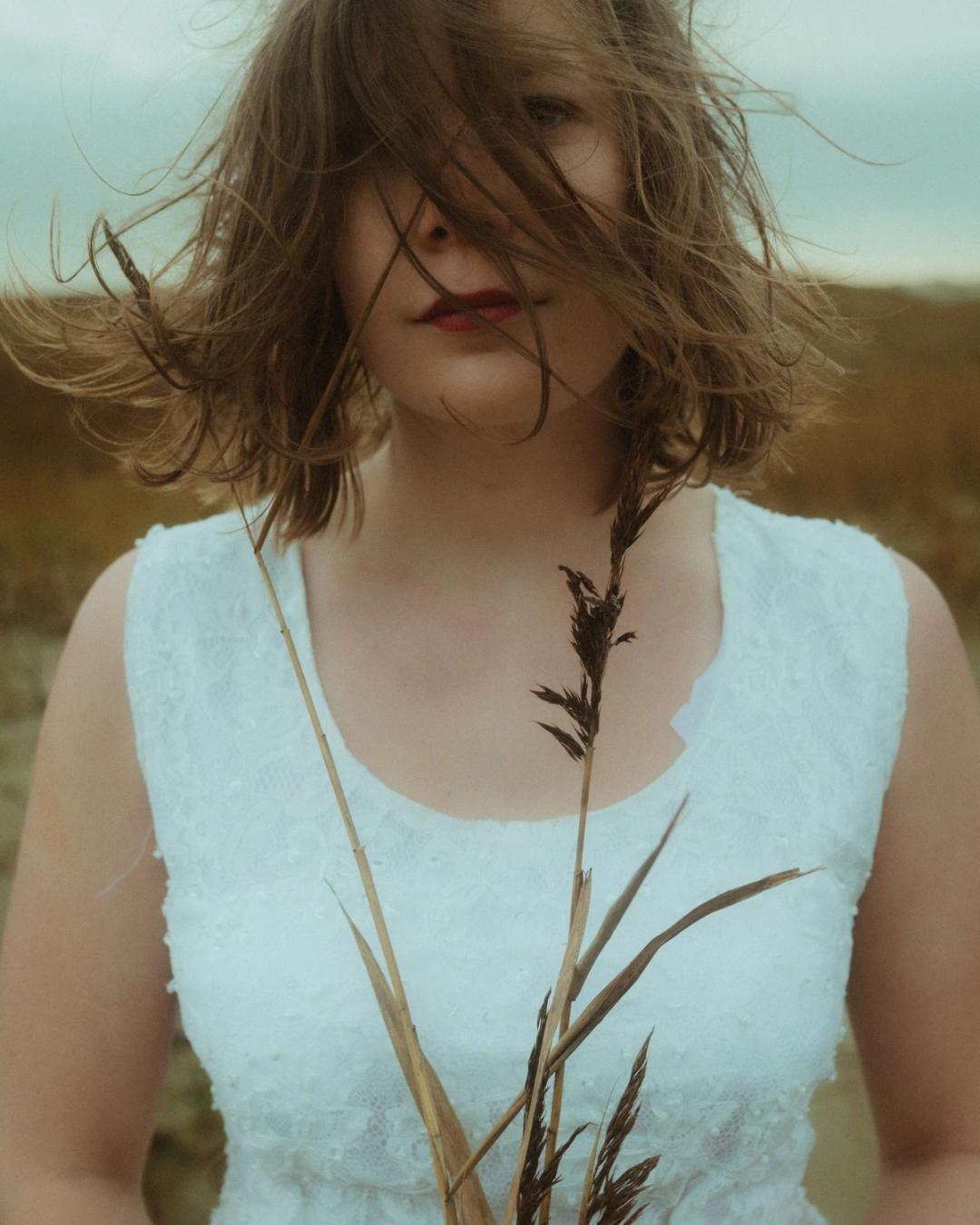 Windswept vertical portrait of Anni behind thin dune reeds.
