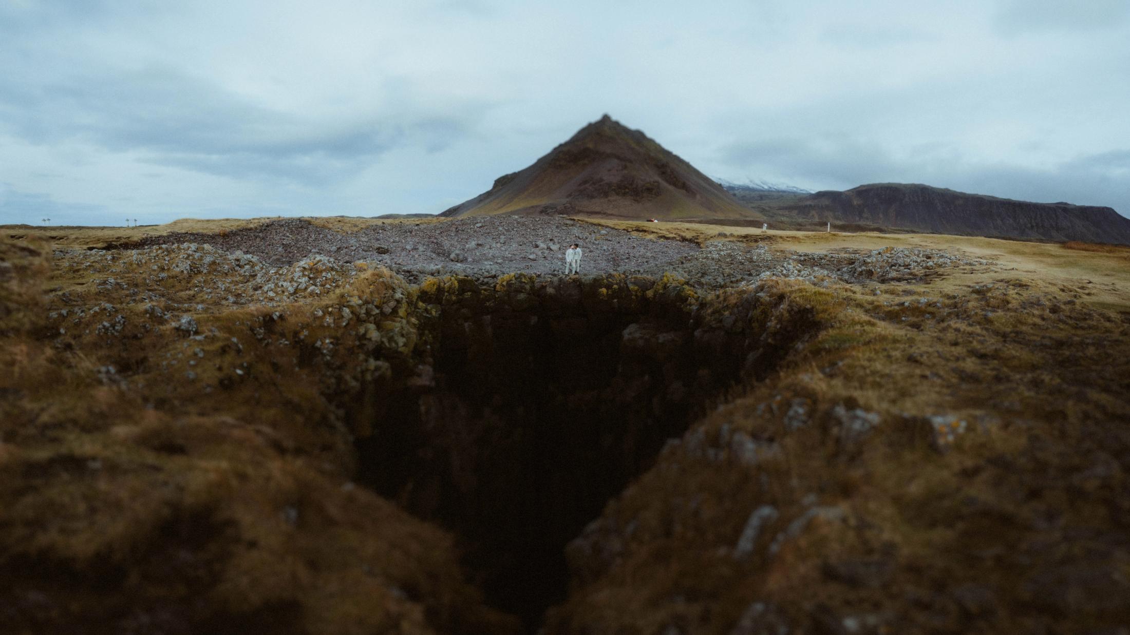 Eine tiefe, moosbedeckte Spalte führt unter grauen Wolken in Richtung Kirkjufell.