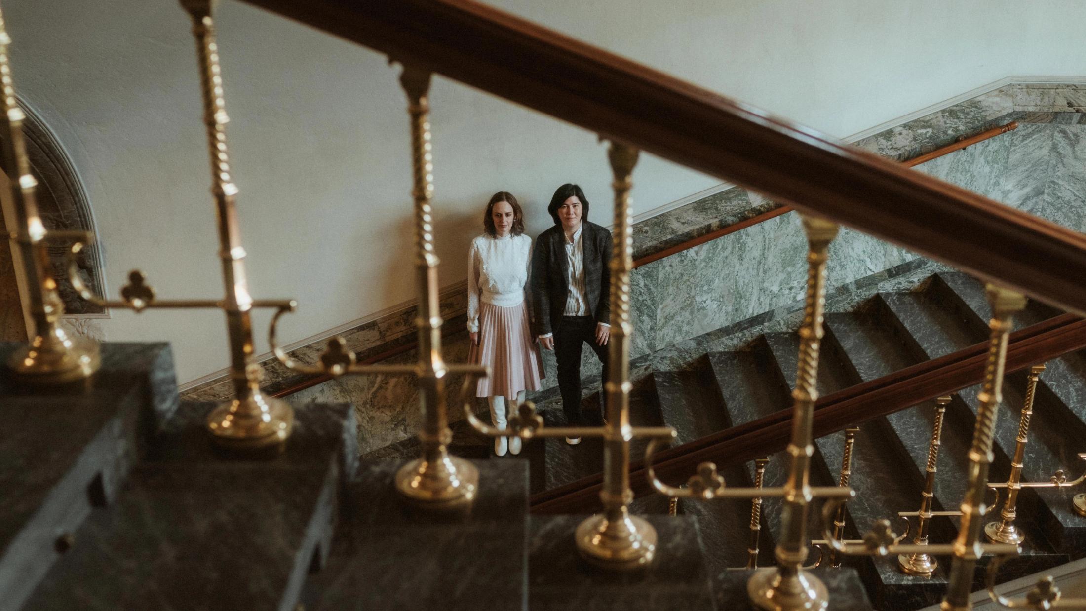 Ari and Pia seen behind brass staircase rails
