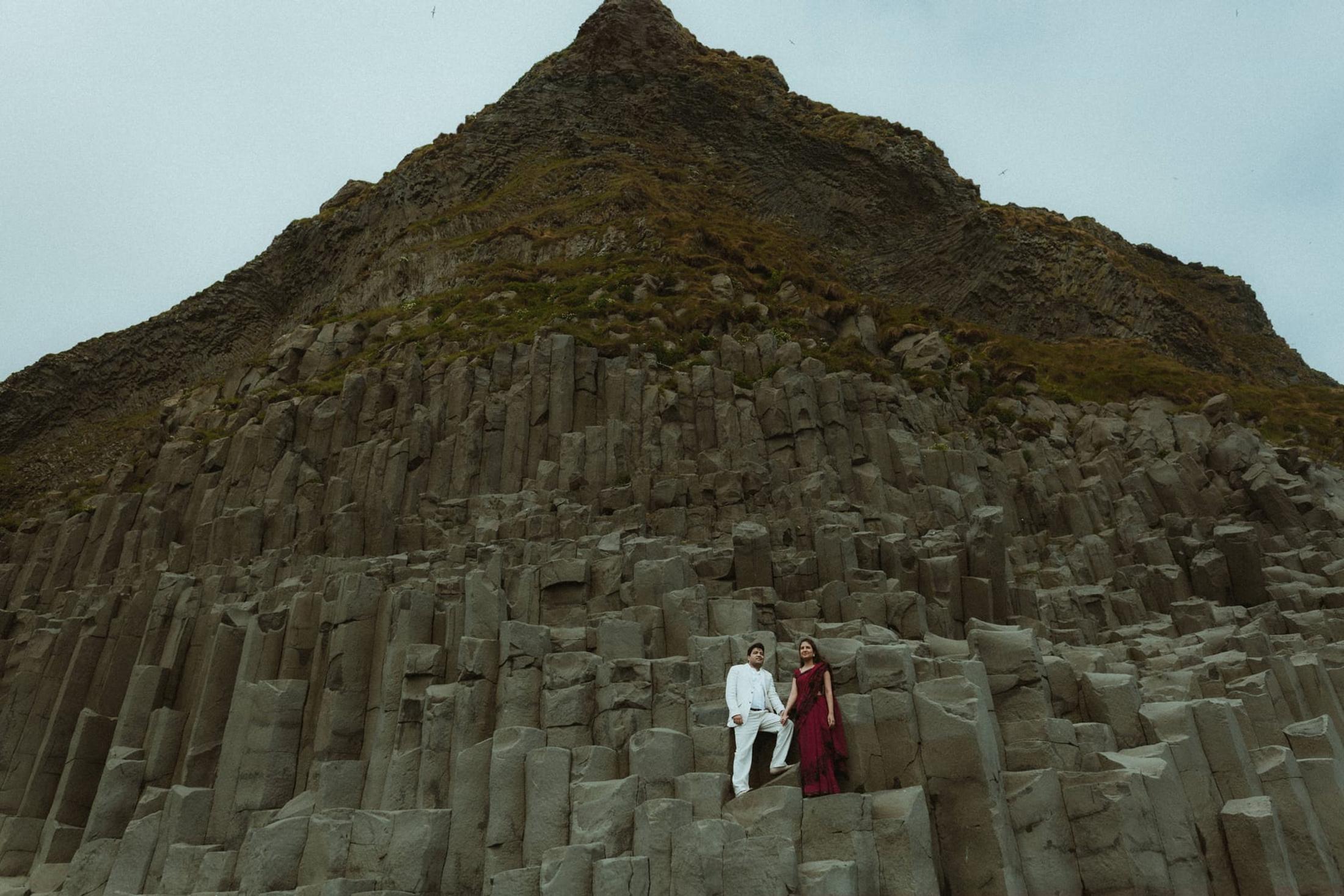 Two people standing beneath a hillside of basalt columns at Reynisfjara.