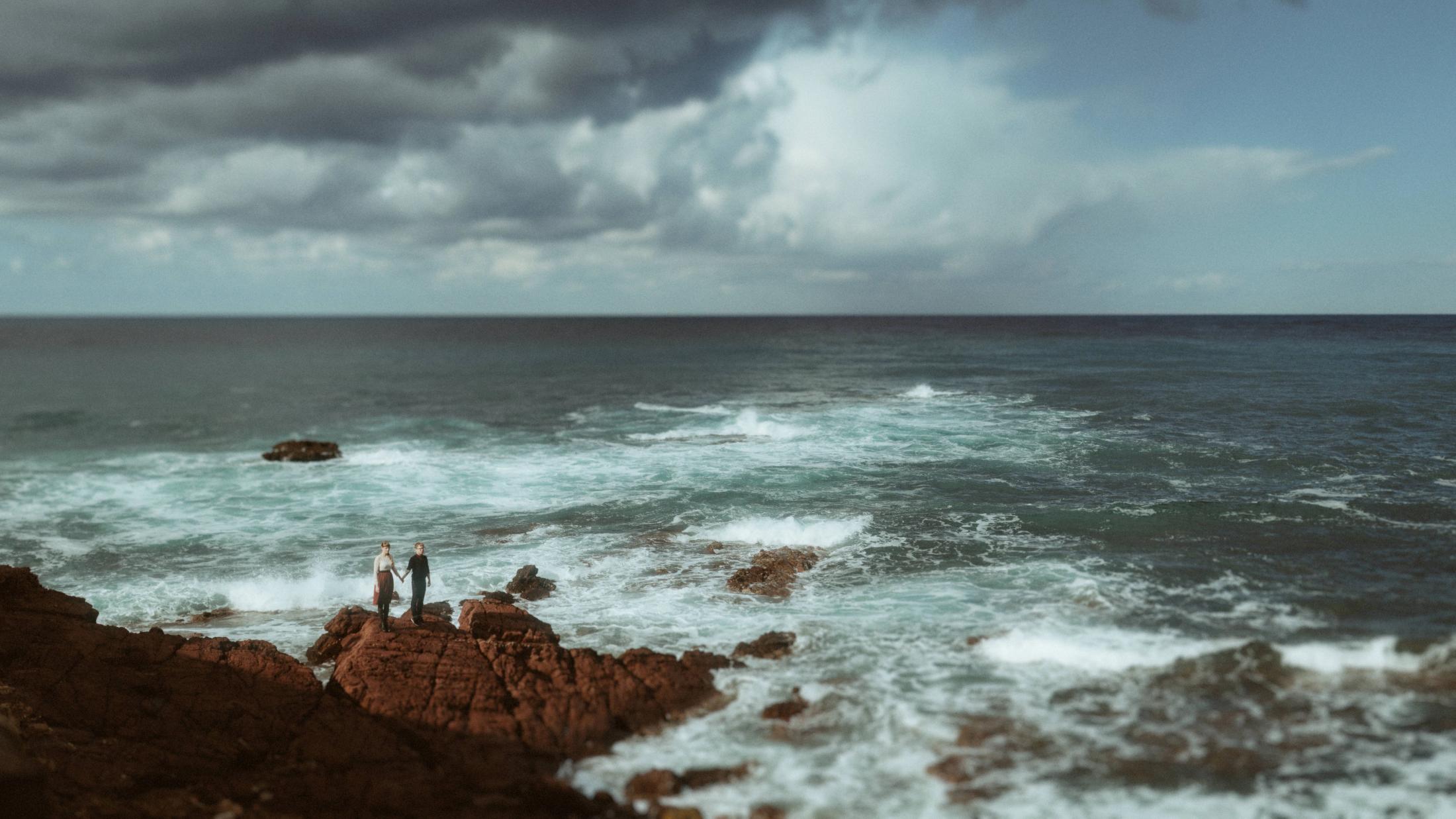 Yannic and Susan stand as small figures on a wide rocky coast.