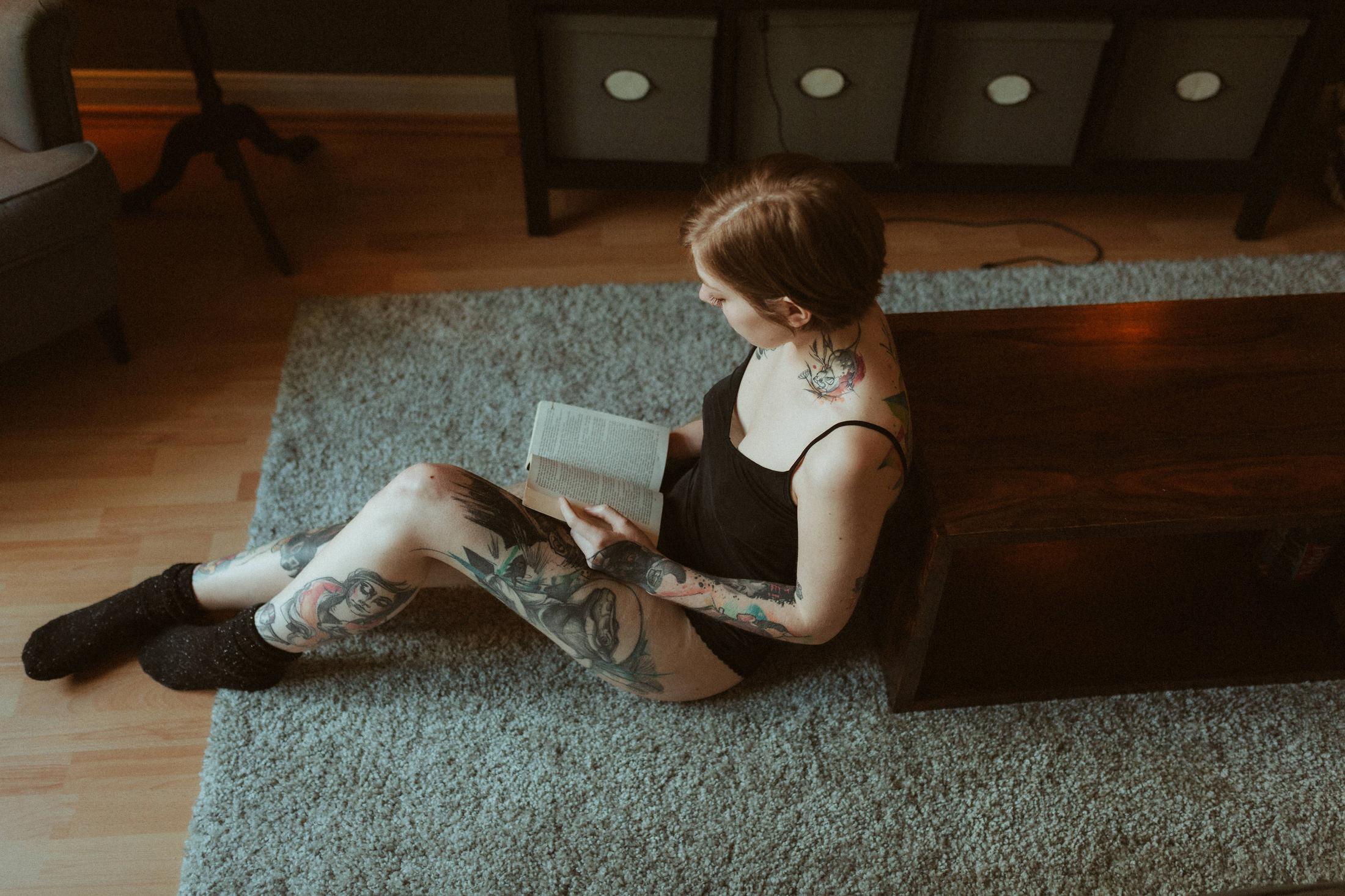 Anki sits on a rug reading a book beside a low wooden chest.