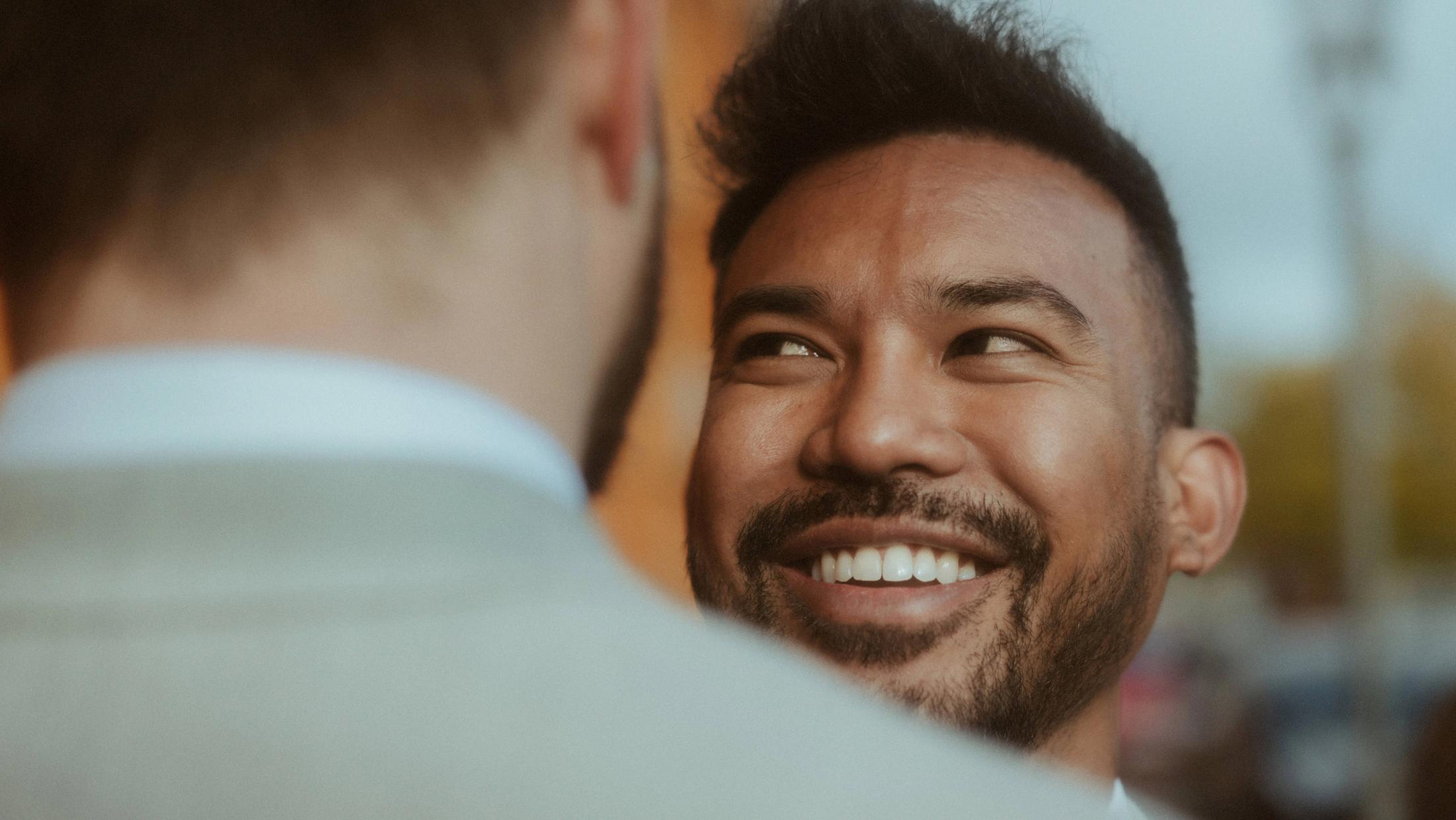 Kris smiles over Ilya's shoulder in a close evening portrait.