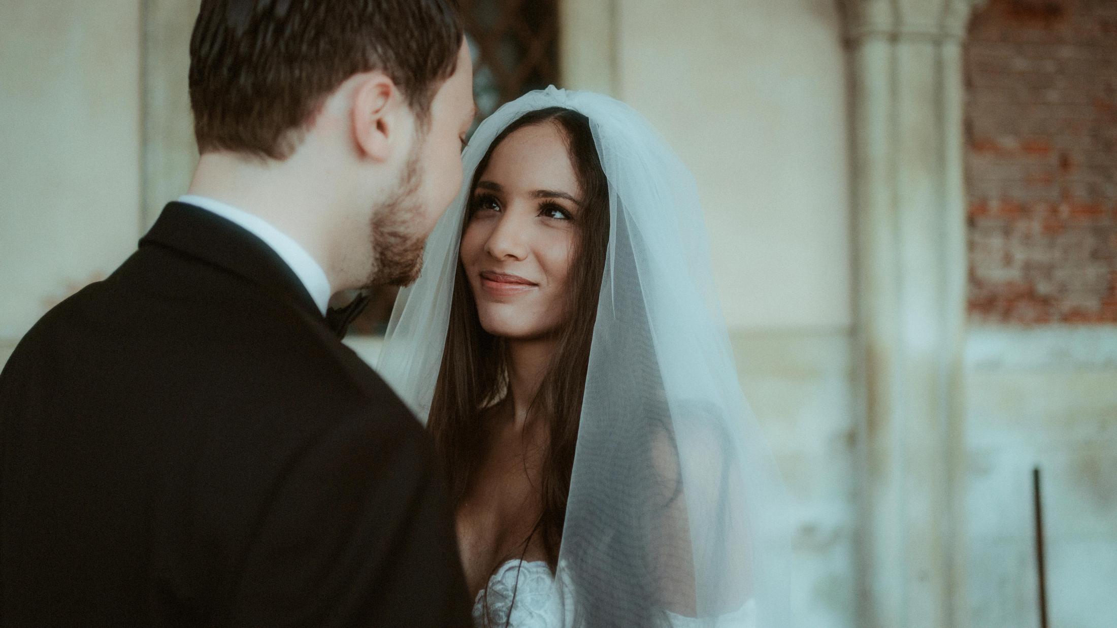 The couple looks at each other closely beneath the bride's veil.